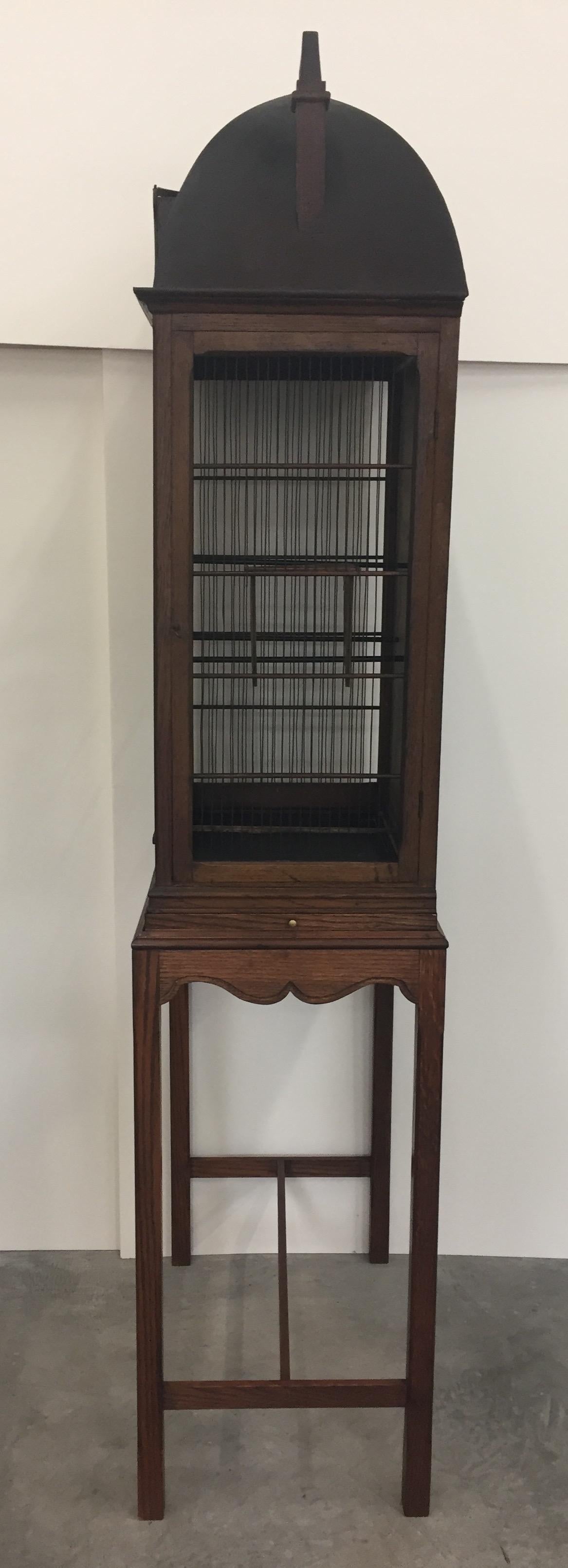 A stunning sculptural large birdcage having an intricately detailed roof, hand painted backdrop, mahogany stand with pull out platform, and working parts to house some lucky chirpers. 

