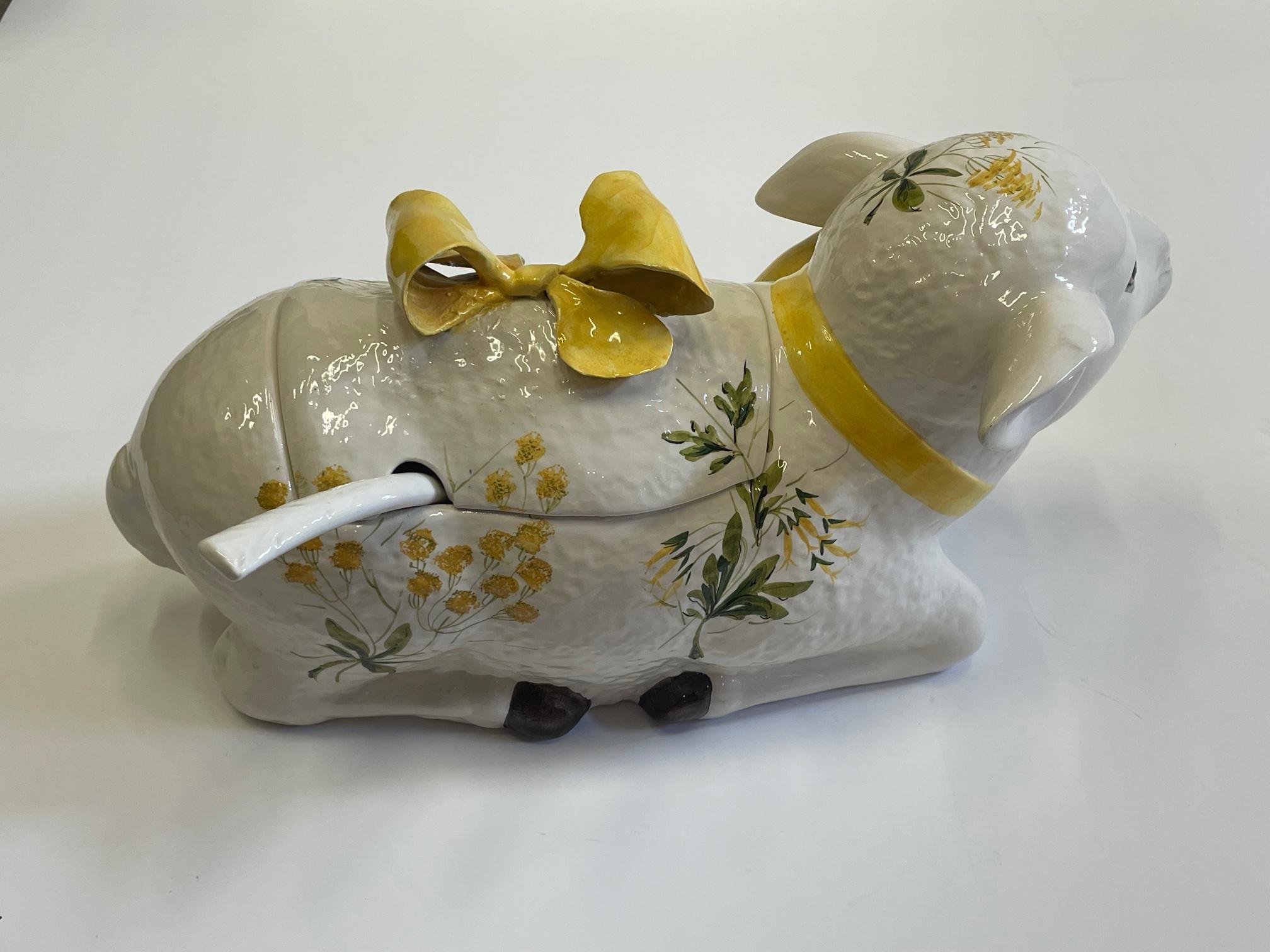 An adorable Italian ceramic vintage tureen in the shape of a lamb in repose, having yellow and green decoration with white background. The lamb is adorned with bows around the neck and on top. Spoon is included.