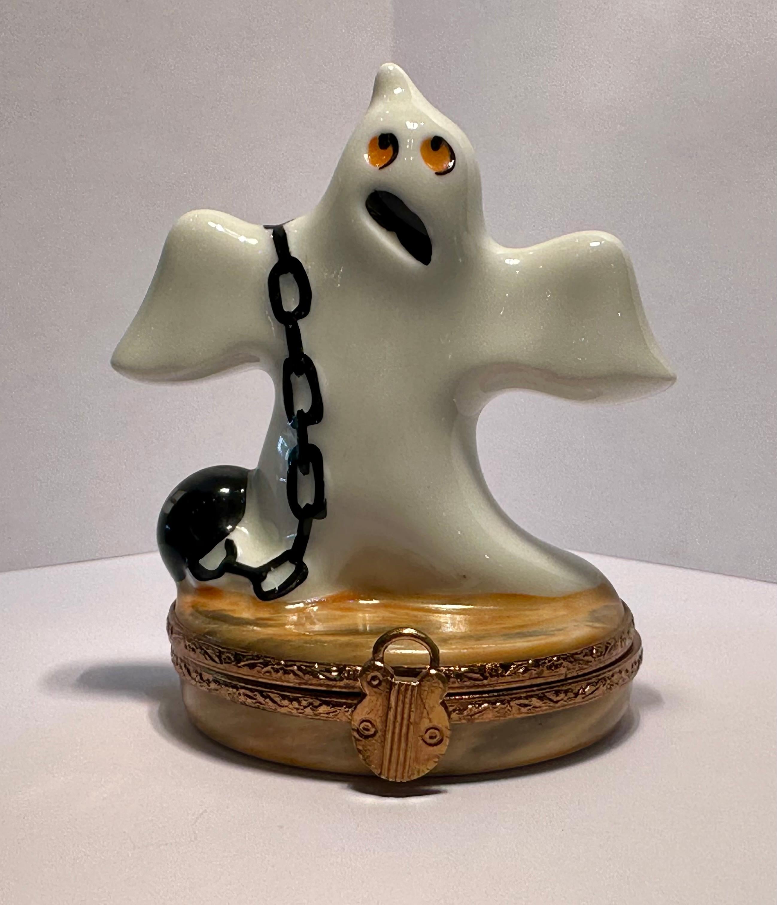 Collectible and whimsical, limited edition Limoges porcelain Halloween motif miniature trinket box is handmade and hand painted in France and features an adorable and very expressive ghost with big orange oval shaped eyes and a black mouth open,