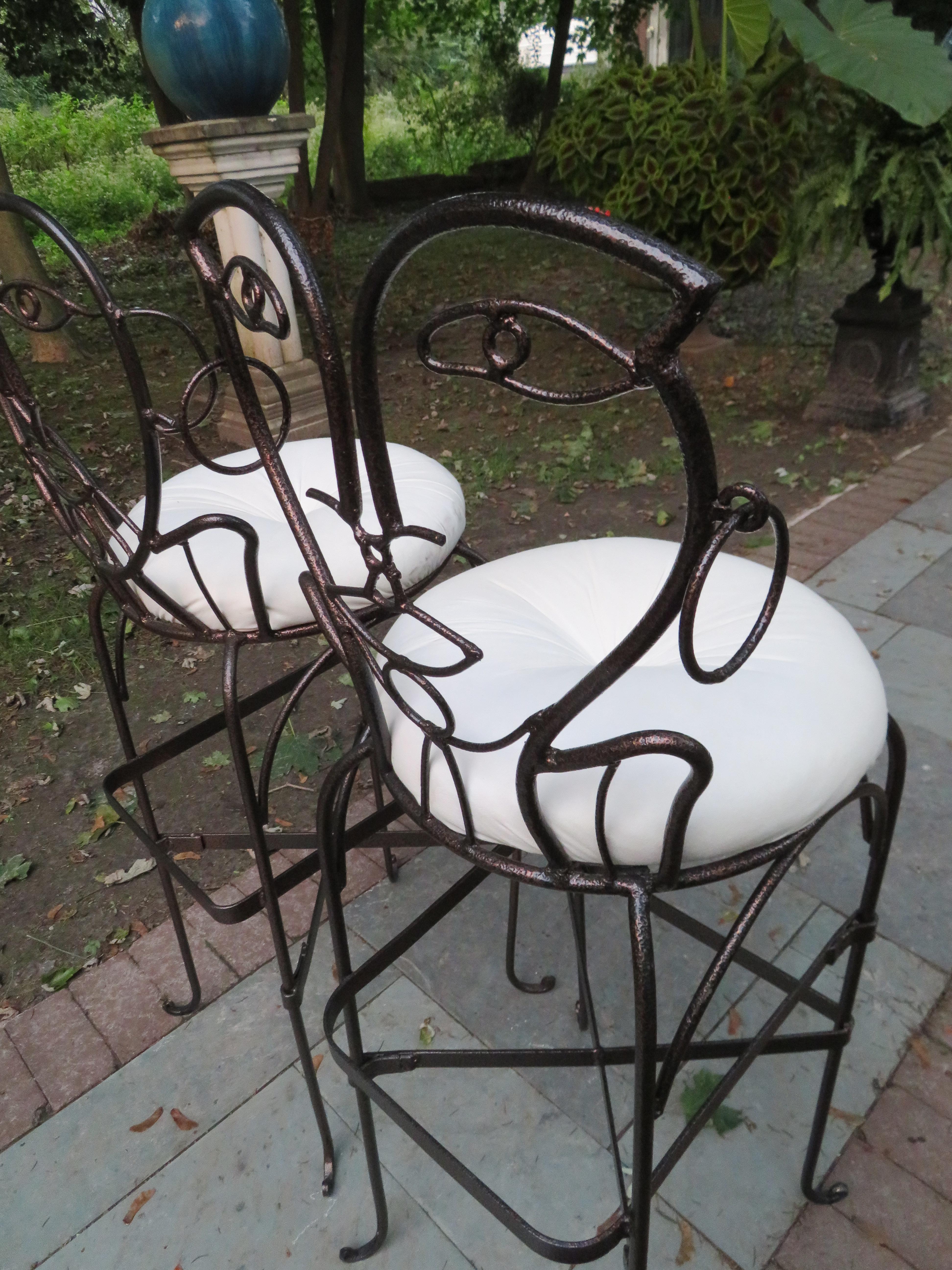 Whimsical pair of wrought and glazed iron barstools with round metal upholstered seats and figurative backs in the shape of a man/woman stylized face. Similar to wrought iron furniture by metal artist John Risley. We have a total of 3 sets or 6