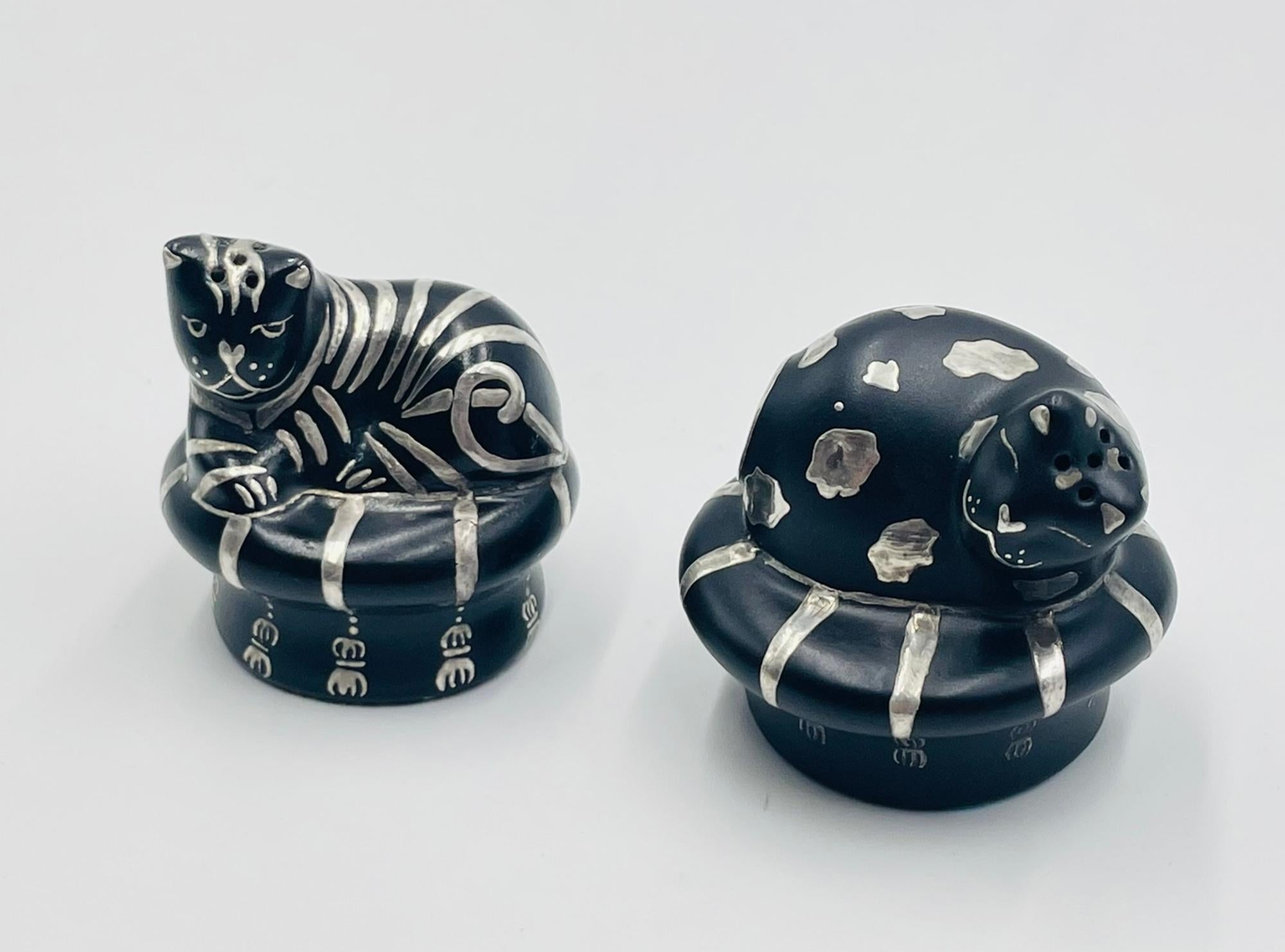 Charming and full of personality, this pair of cat-shaped salt and pepper shakers was designed and handcrafted in Taxco, Guerrero, Mexico by renowned silversmith Emilia Castillo in 1996. Each piece is meticulously made in black porcelain with inlaid