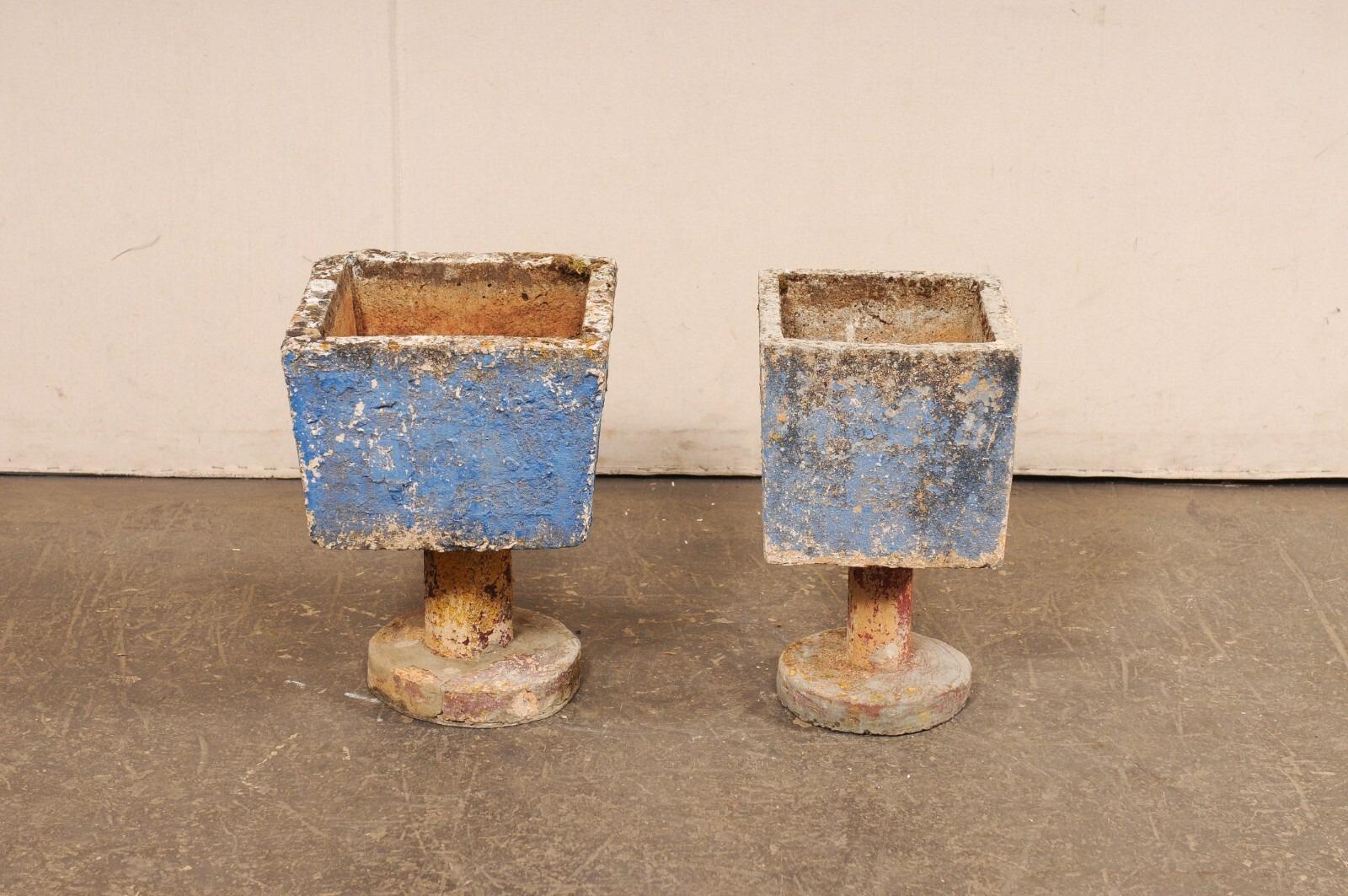 A Spanish near-pair of cast-stone planters, with their original paint, from the mid-20th century. These playful garden planters from Spain have square-shape bodies which are raised on cylindrical pedestals, and supported on a round platform base.