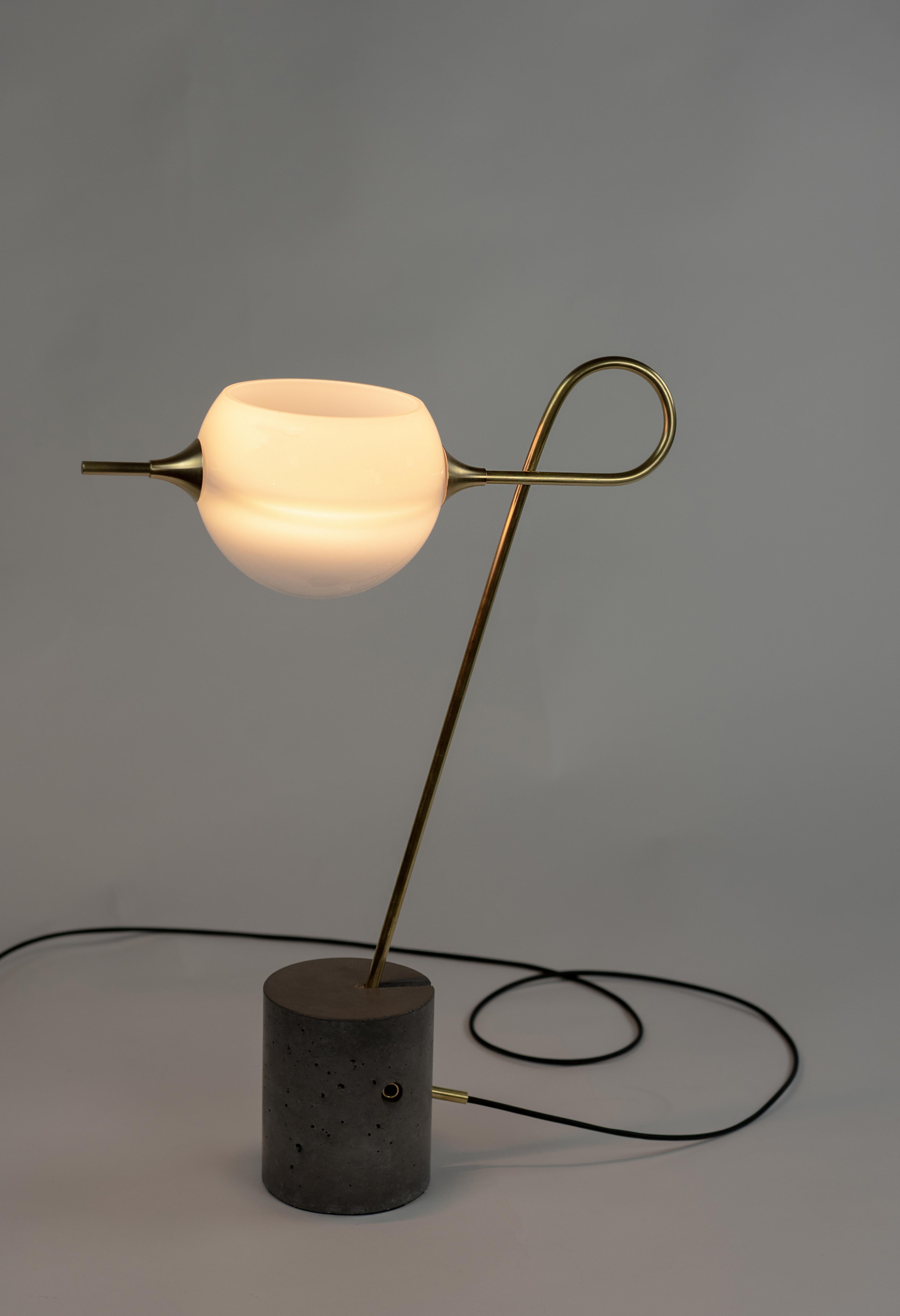 The Whiplash Desk Lamp features a cylindrical cement cast base. The hand-formed brass arm is secured by a brass dowel. The fixture has a single glass Whiplash shade,
each shade is hand-blown and illuminated by a dimmable LED. Shade can be faced up