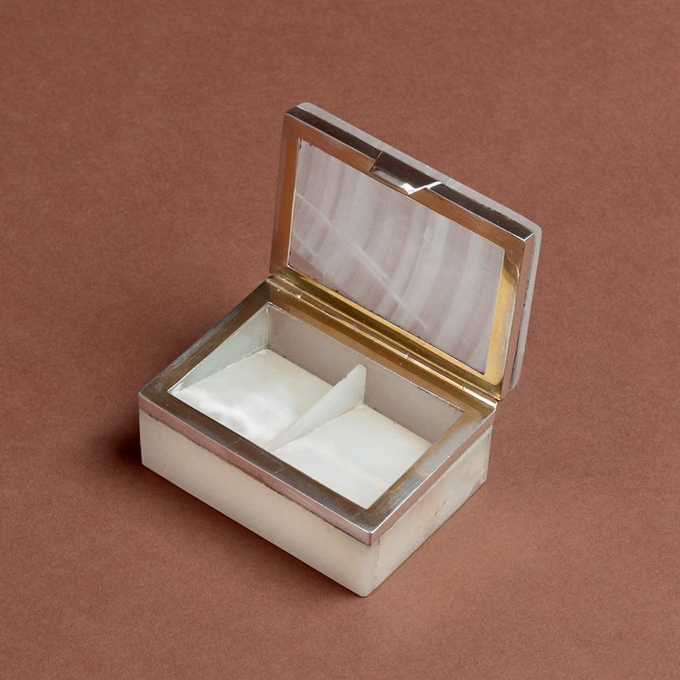 A stylish small box made from white Agate with grey striations running through the stone. A sterling silver hinge and frame join the top and bottom sections. Originally used as a stamp box, hallmarked London 1919.

Dimensions: 18 cm/3 inches