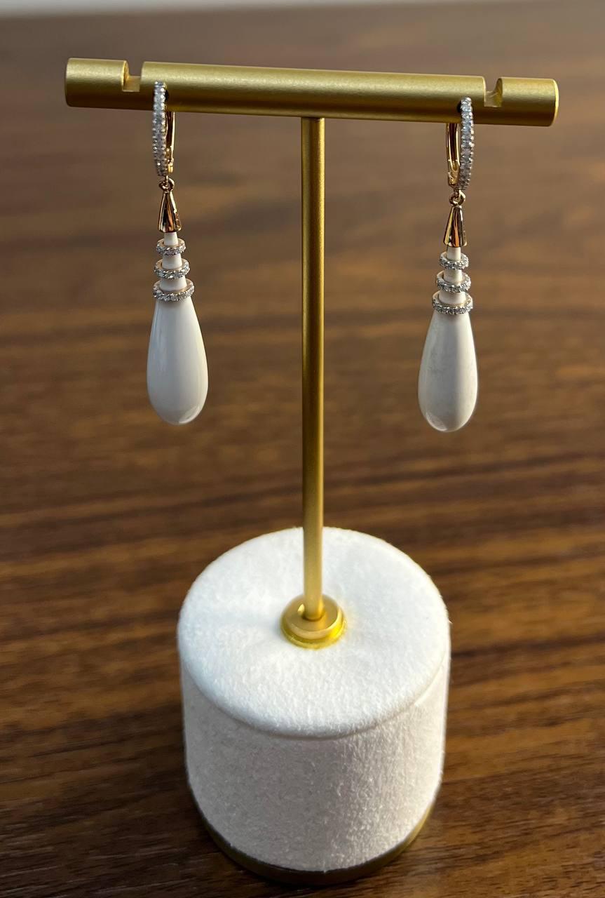 A refined pair of earrings, each featuring a teardrop-shaped white agate gem center stones, accented with three circular bands encrusted with small, sparkling diamonds of G/VS Quality. The earrings are suspended from 18K Rose Gold hook, adorned with