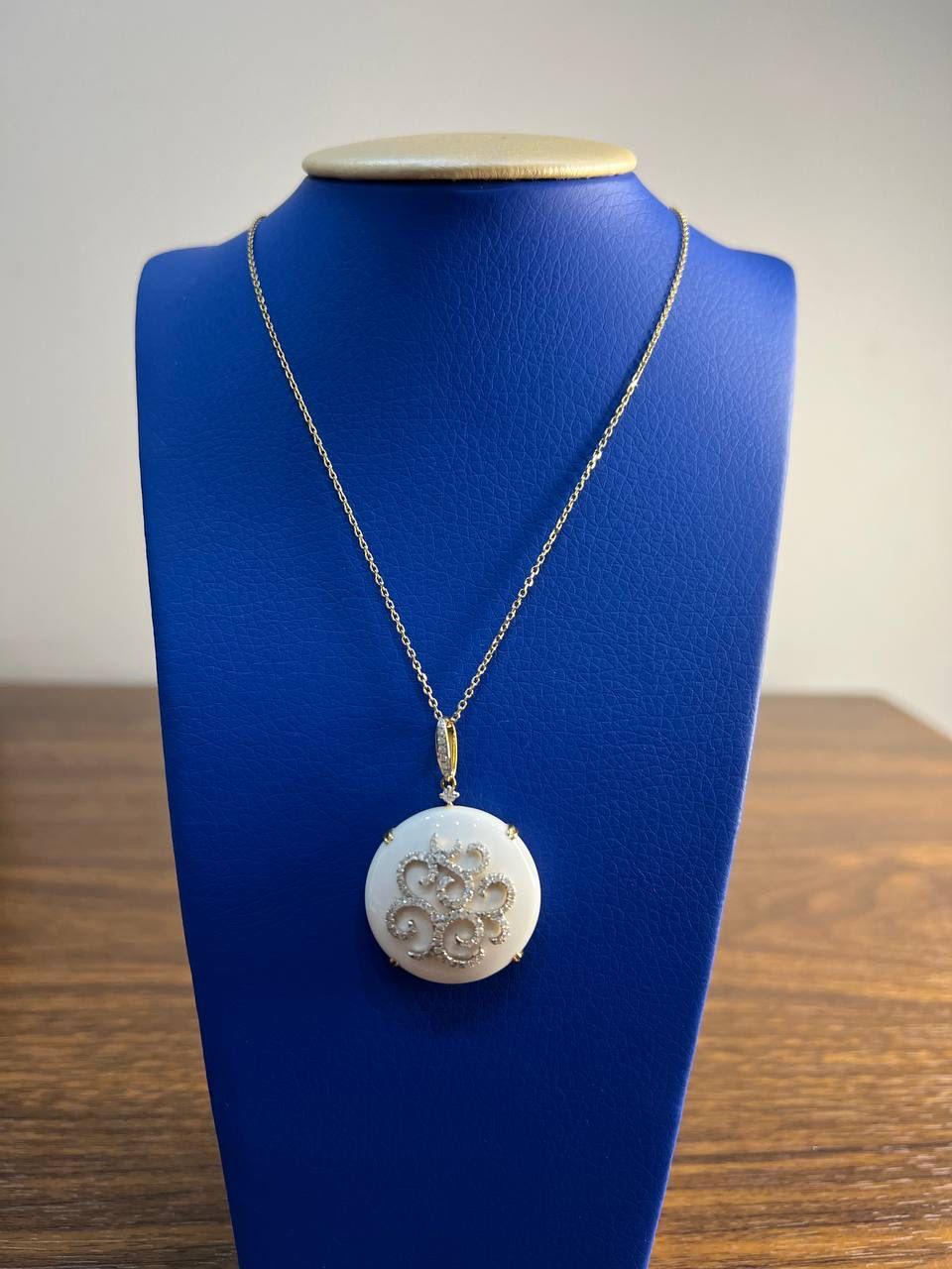 This exquisite necklace features a delicate chain with a round pendant. The pendant showcases an intricate swirling design adorned with sparkling diamonds, set against a smooth white agate center gemstone. The craftsmanship highlights the contrast