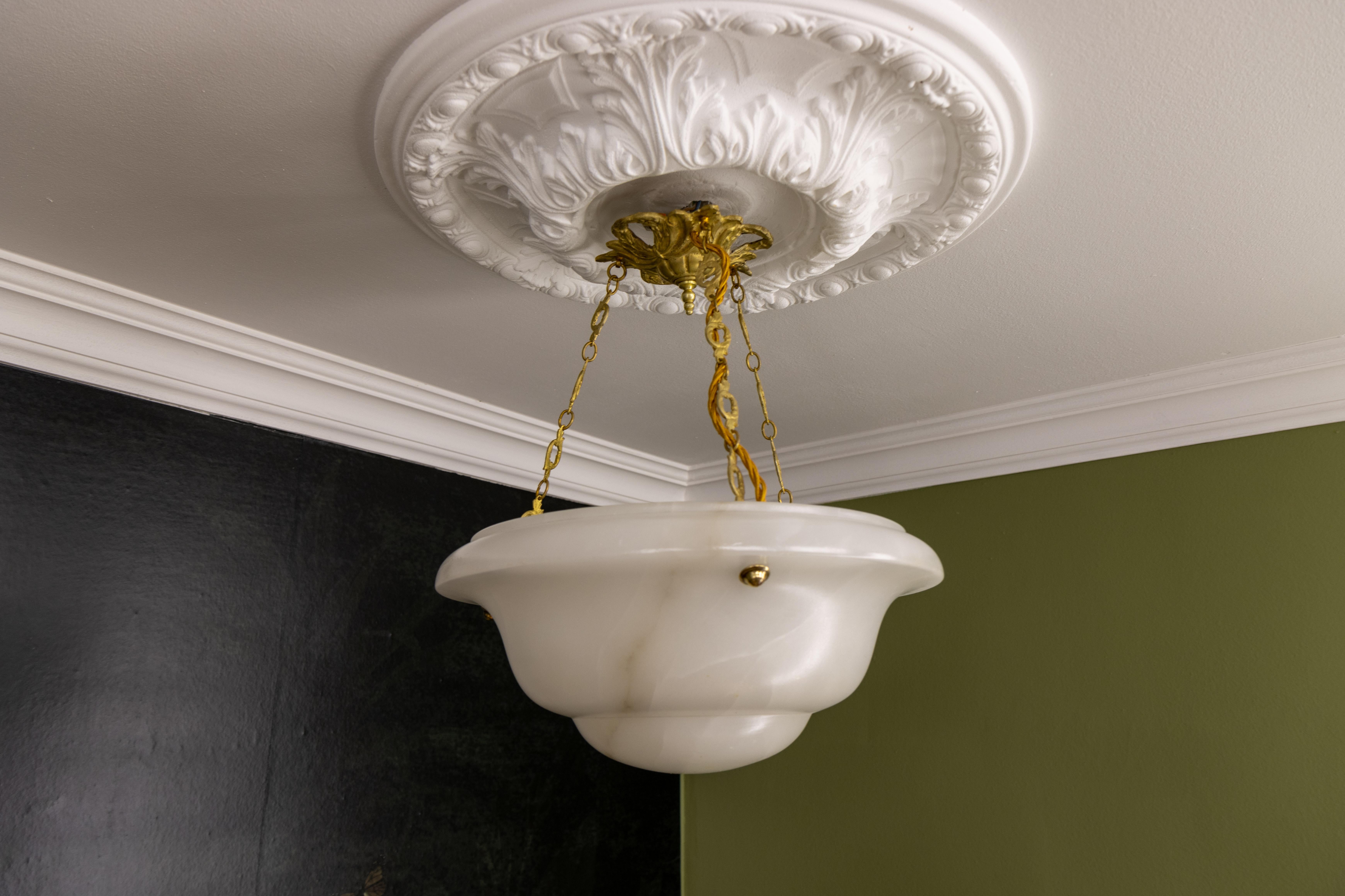 Art Deco white alabaster pendant light with slight dark brown veins.
This adorable alabaster pendant ceiling light fixture dates from circa the 1930s. It features a beautifully shaped slightly veined white alabaster bowl suspended by three