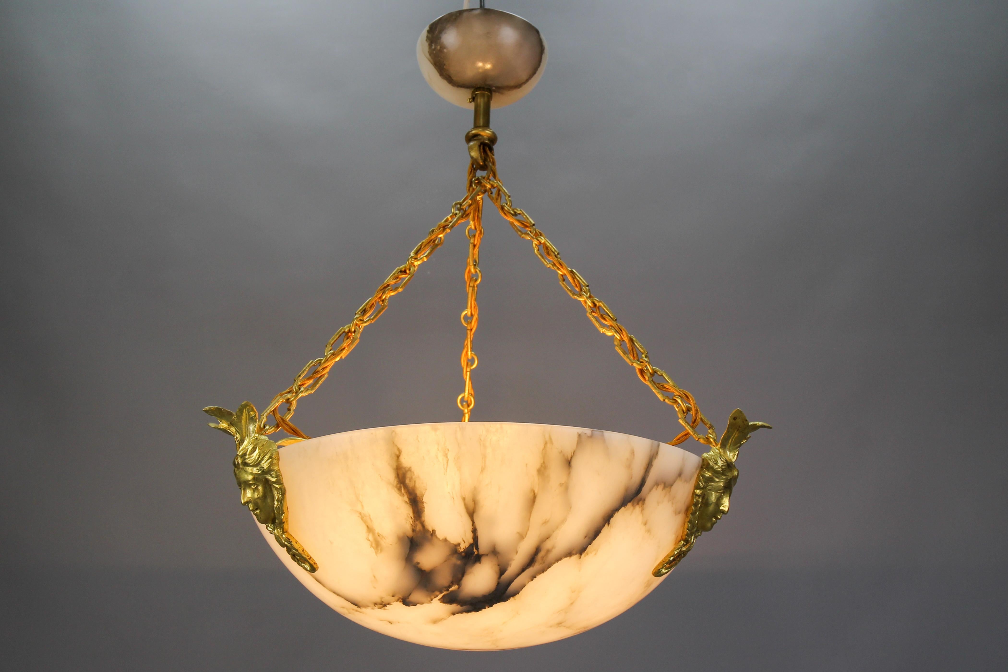 Louis XIV-style black veined white alabaster pendant light with bronze fixtures.
An adorable alabaster pendant light fixture from circa the 1920s. This antique and beautifully veined white alabaster bowl is suspended by three massive bronze chains,