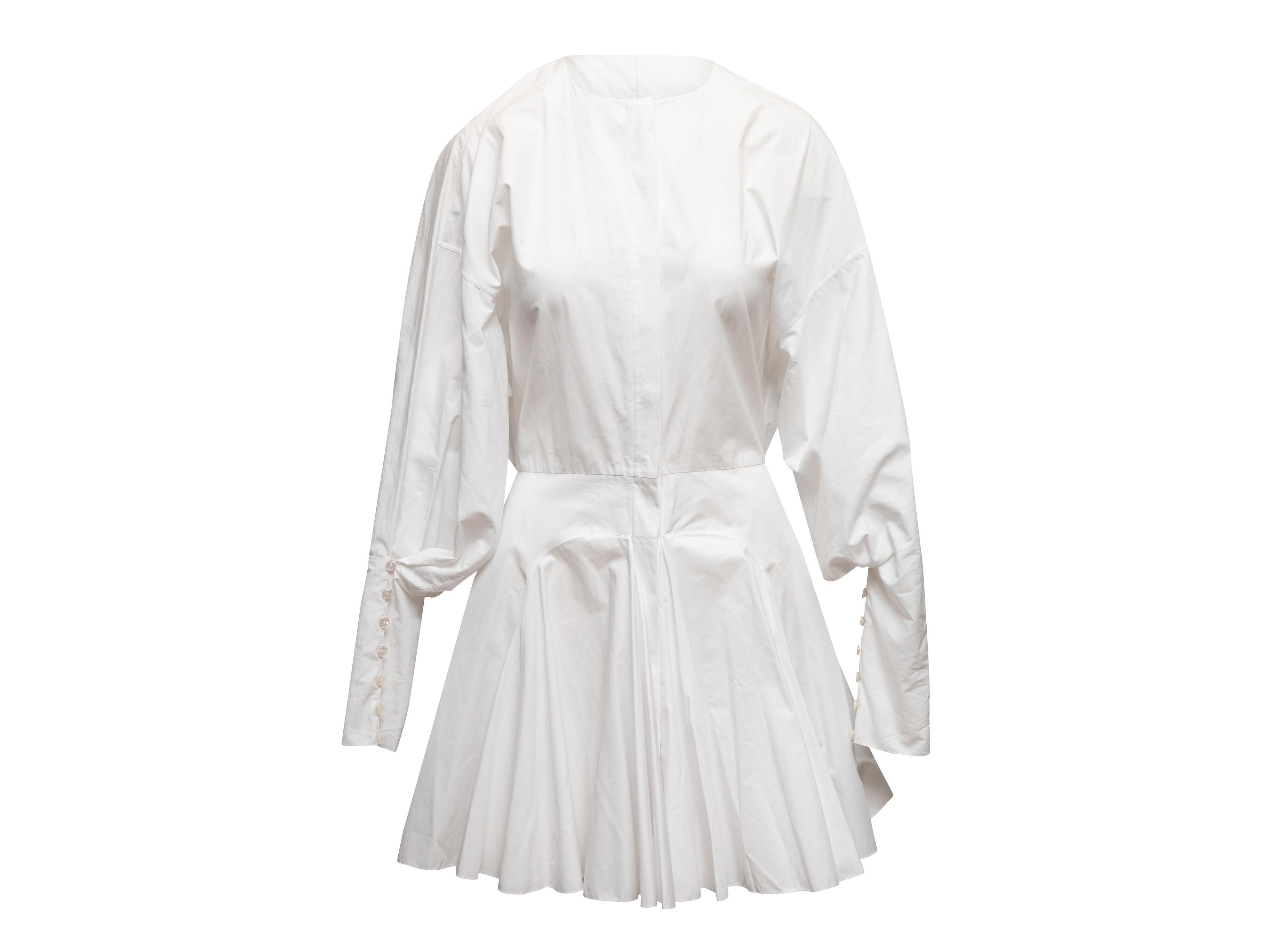 Mini robe à manches longues en coton blanc signée Alaia. Col ras du cou. Plis sur la jupe. Fermeture par boutons sur le devant. Poitrine 36