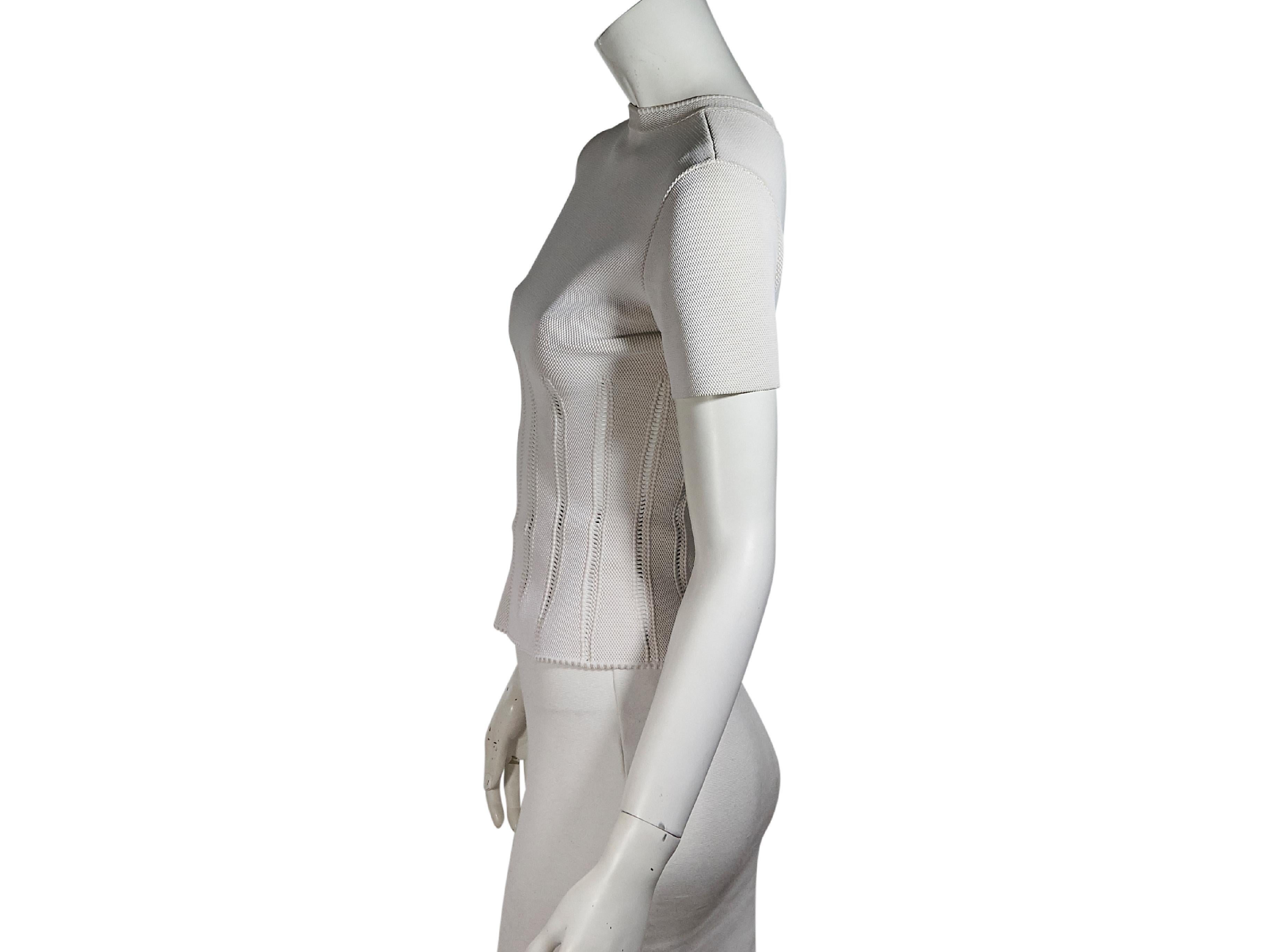Product details:  White stretch top by Alaia.  Accented with cutout stripes.  Roundneck.  Short sleeves.  Exposed back zip closure.  Silvertone hardware.  33