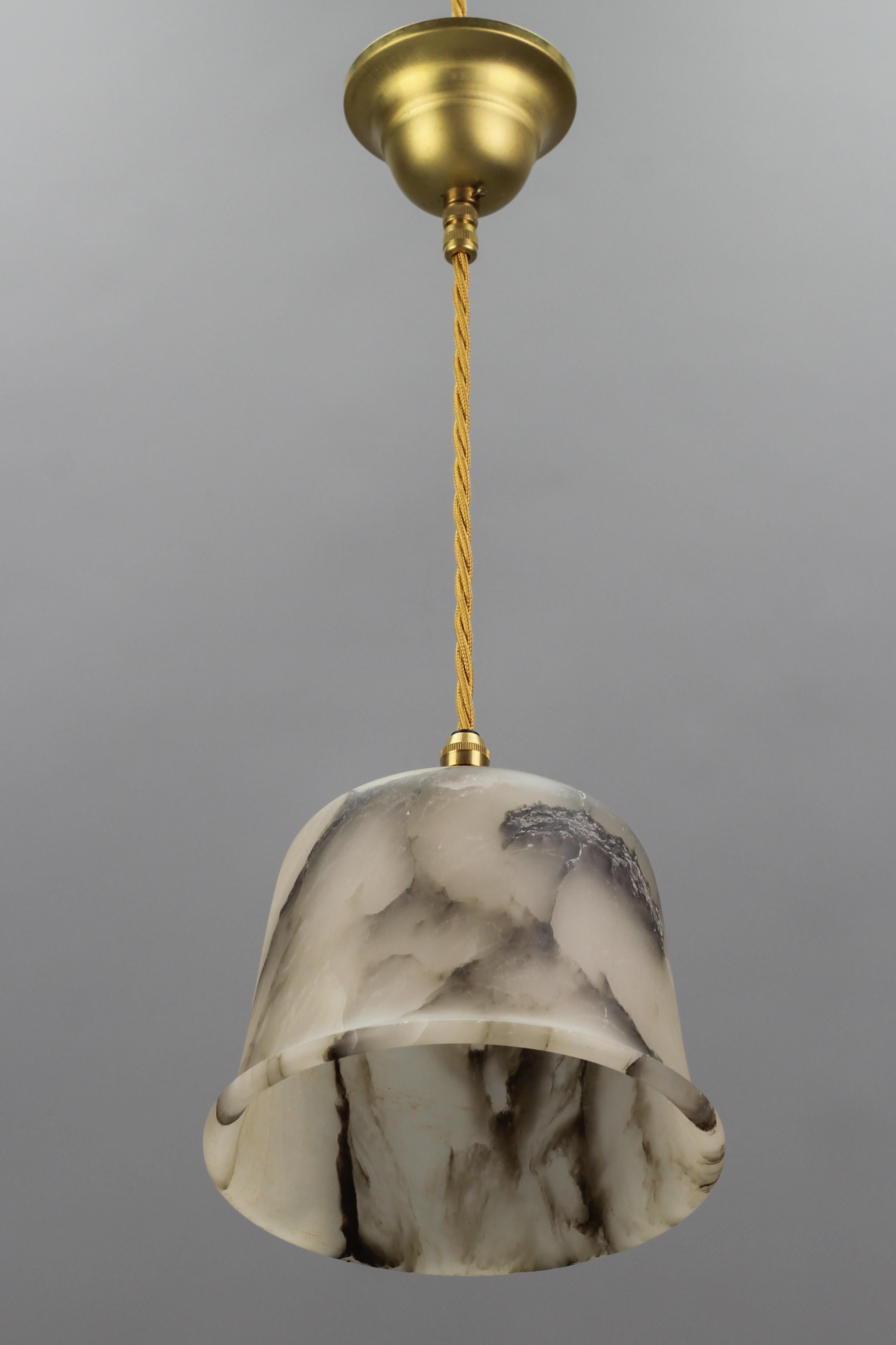 Adorable and compact Art Deco alabaster pendant light.
The beautifully veined white and black alabaster lampshade is suspended from a brass canopy. The light shining through the white stone with dark brown and black veins is warm and atmospheric,