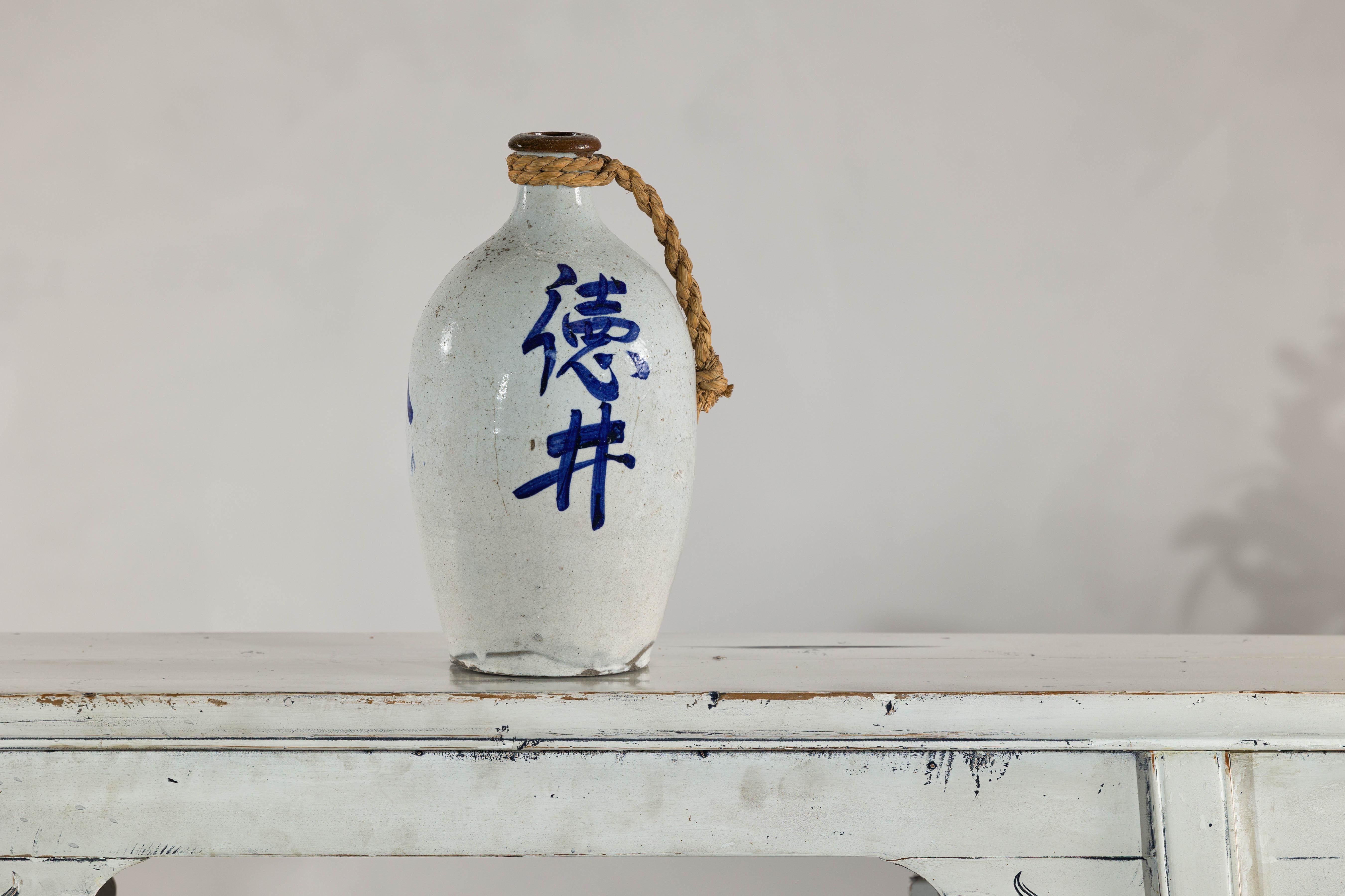 Con la sua superficie organica, la forma tradizionale e la vivida calligrafia blu, questa brocca in ceramica vintage è un accento di carattere per interni sia moderni che tradizionali. Il vaso presenta uno smalto grigio-bianco leggermente maculato