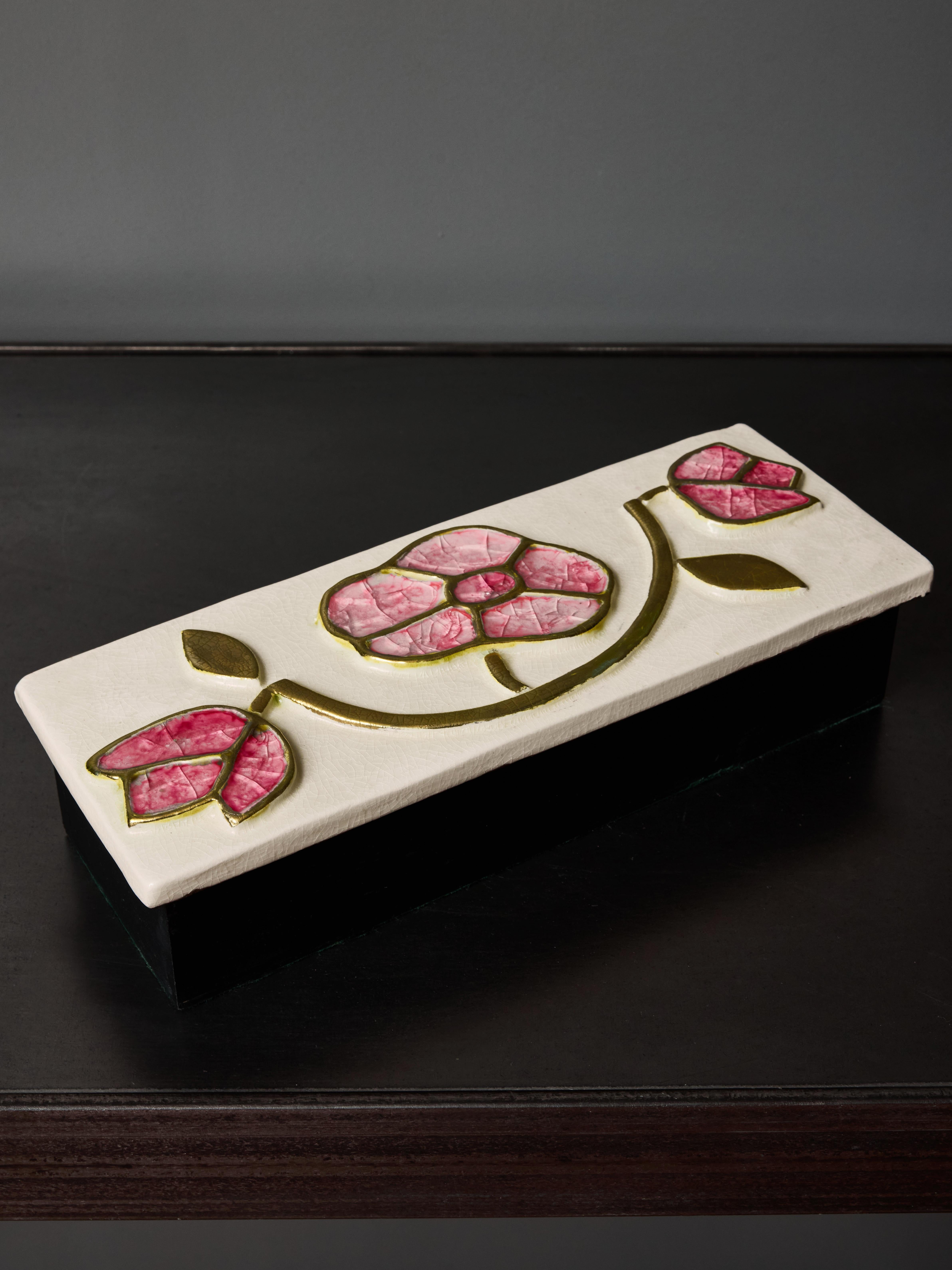 Caja rectangular de madera con tapa de cerámica de Mithé Espelt. La cerámica luce un fondo de esmalte crema y motivos florales en vidrio rosa fundido con revestimiento dorado craquelado.

Bibliografía: Mithé Espelt, el lujo discreto de lo