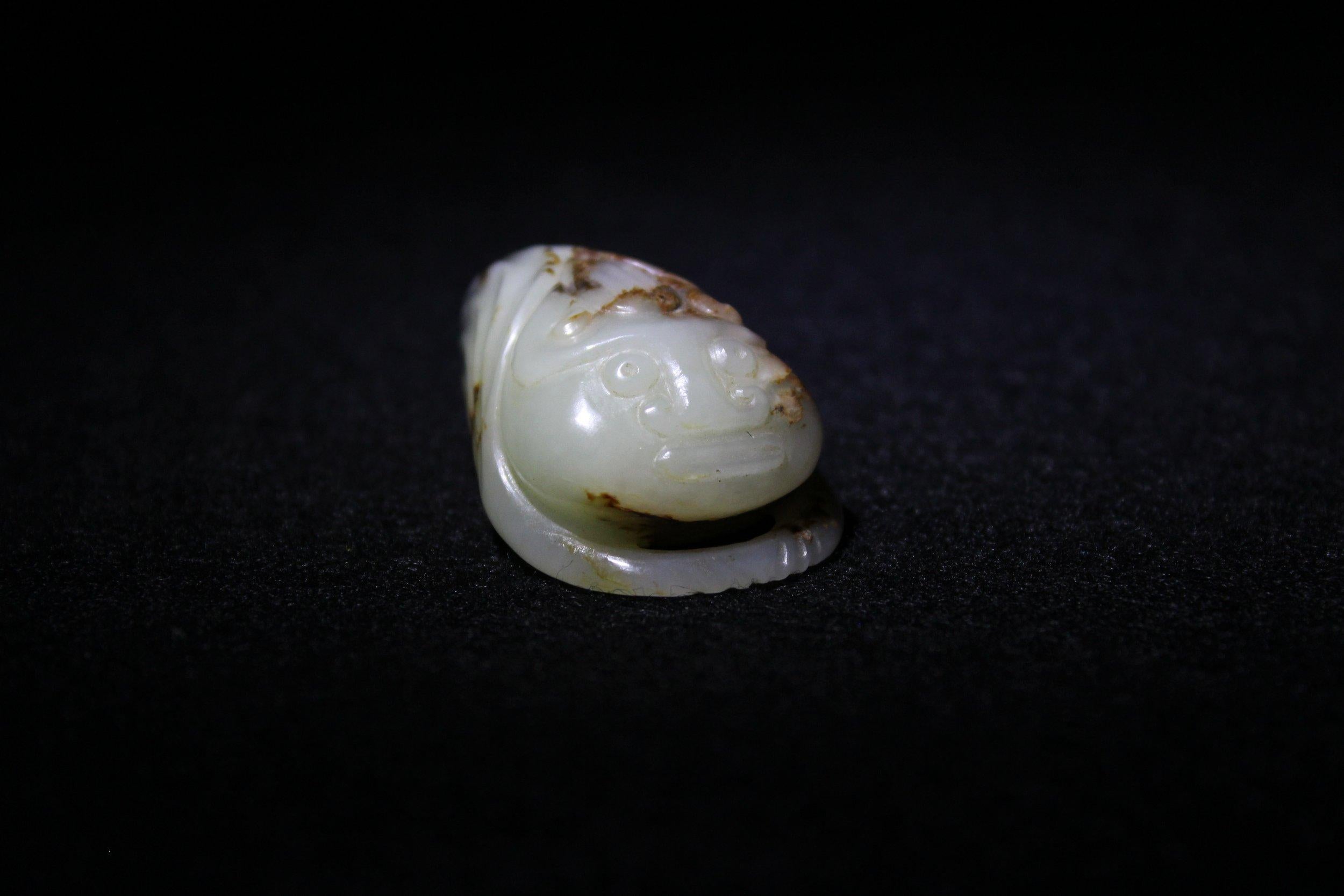 Esta cigarra, tallada en jade rojizo de Hetian, es arcaica y recuerda el estilo de las cigarras de jade de la dinastía Han. Esta pieza presenta el rostro de una bestia mítica, con globos oculares redondos y voluminosos, cejas curvadas, nariz ancha y