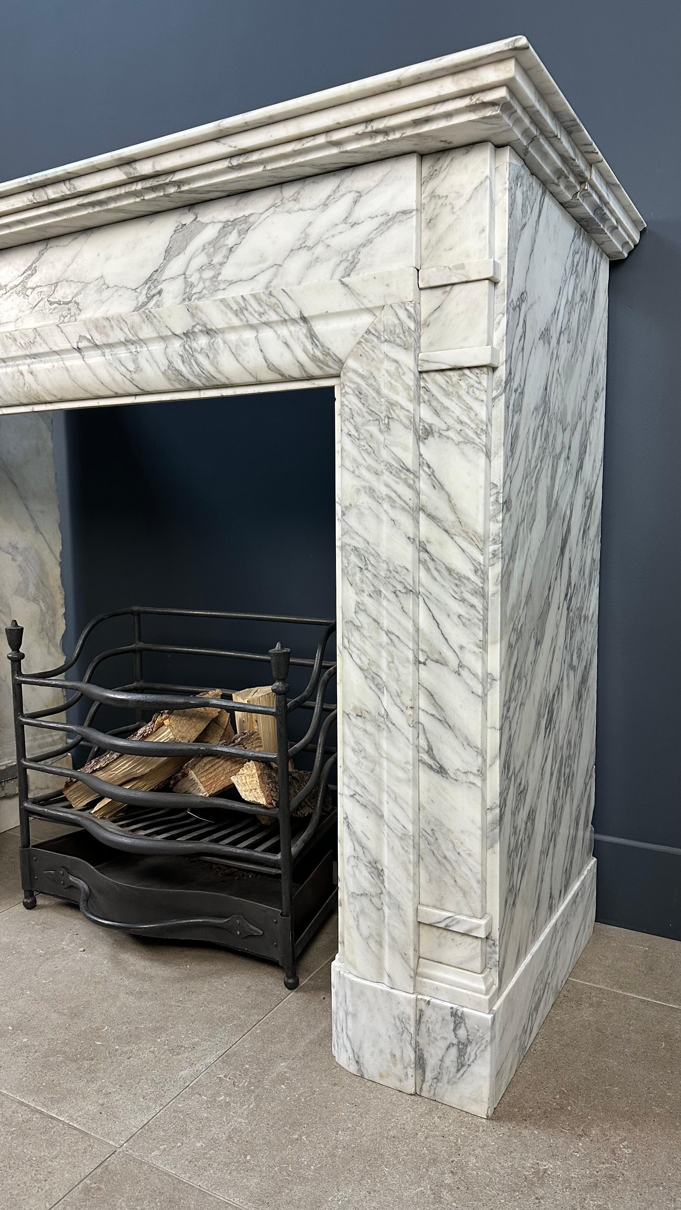 Behold, an Antique Art Deco Fireplace, resplendent in its exquisite veined white marble. This timeless masterpiece traces its origins to a magnificent mansion nestled in the heart of Amsterdam, just behind the municipal museum, where it once graced