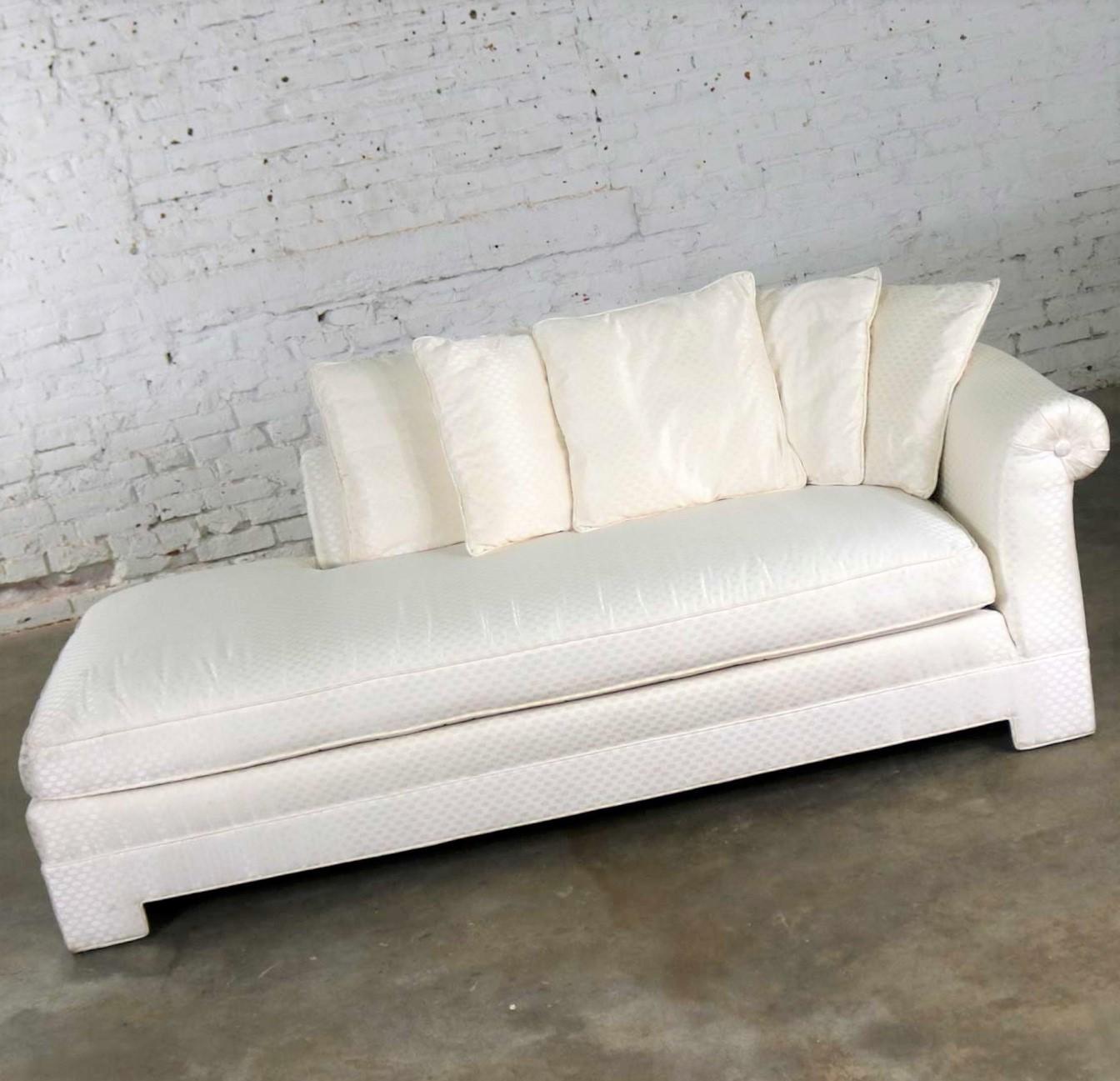 Elegant vintage chaise lounge in an Art Deco or Hollywood Regency styling having loose pillows and a rolled single arm and back and covered in a white jacquard checked upholstery fabric. It is in wonderful overall condition. Structurally solid and