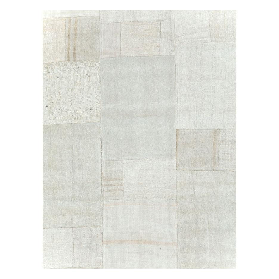 A contemporary Turkish flatweave Kilim large room size carpet handmade during the 21st century in shades of white and beige. This patchwork style rug consists of hand-weaving together several remnants of vintage Kilim carpets from the mid-20th