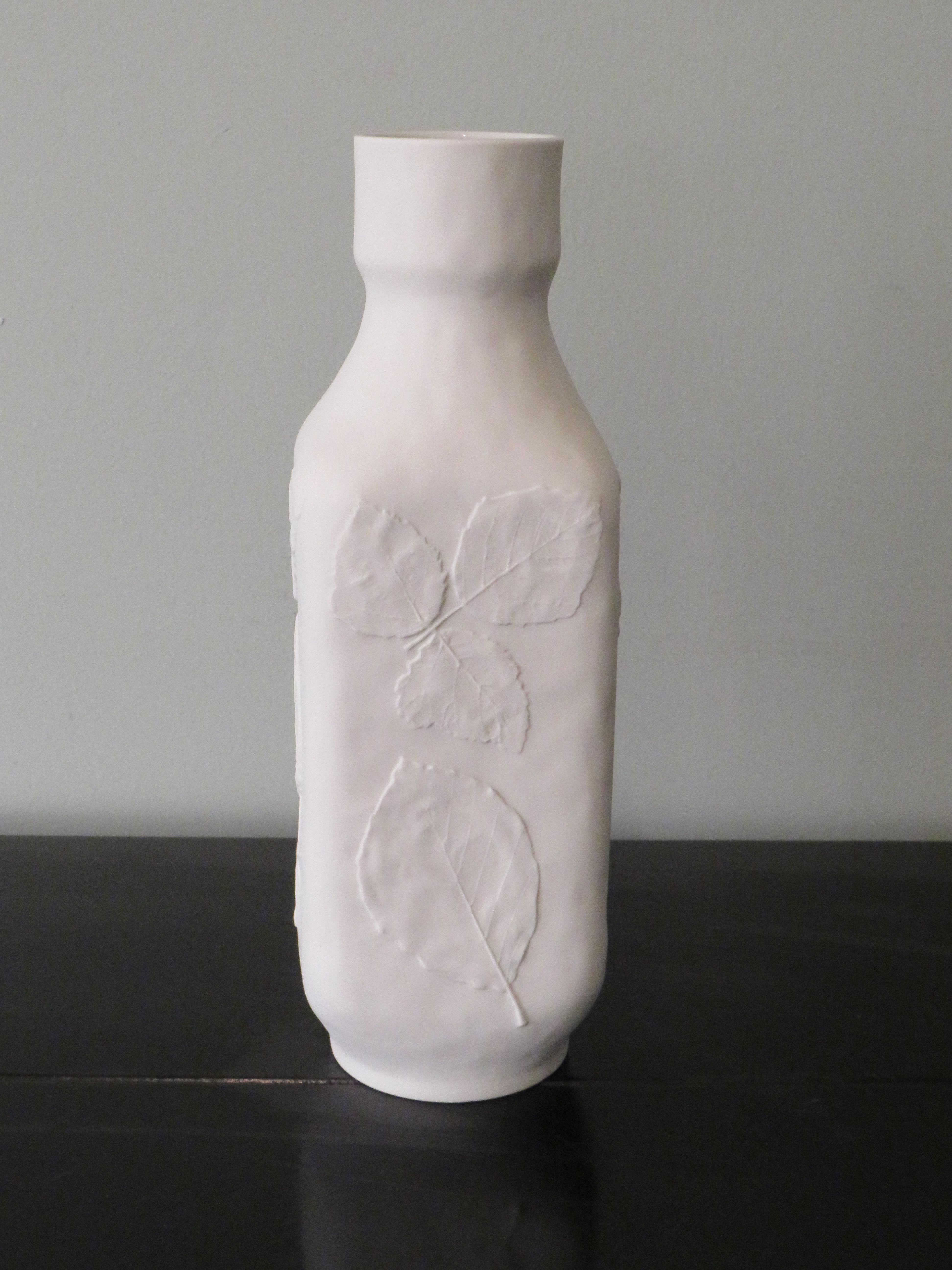 Square vase with rounded corners and on all 4 sides a different embossed floral leaf motif on a vaulted ground. The vase has a matte outside and a glossy inside.
The vase has a mark and number on the bottom.
Measures: The height of the vase is 26