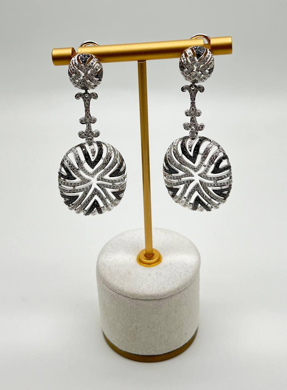 Elegantes pendientes contemporáneos de oro blanco de 18 quilates con diamantes y diamantes negros. Este exquisito par de pendientes está elaborado en oro blanco de 18 quilates. Los pendientes llevan diamantes blancos talla brillante y diamantes