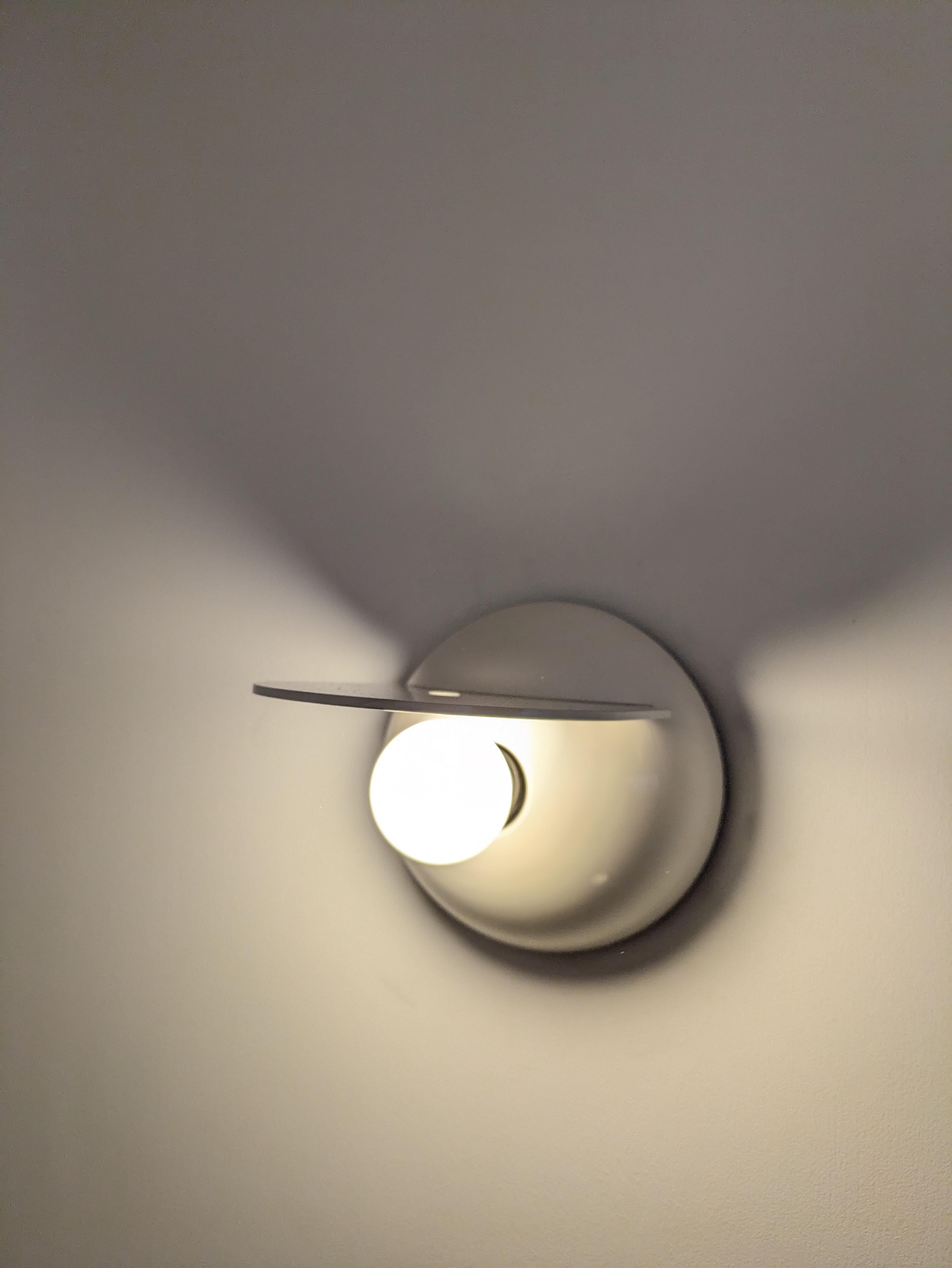 Este aplique Buco (Agujero) es de fabricación italiana y está fabricado por Artemide. Fue diseñada por el diseñador italiano Claudio Dini. 
Es de plástico blanco 🤍 (ABS) sobre un soporte de plástico negro que permite que la parte blanca