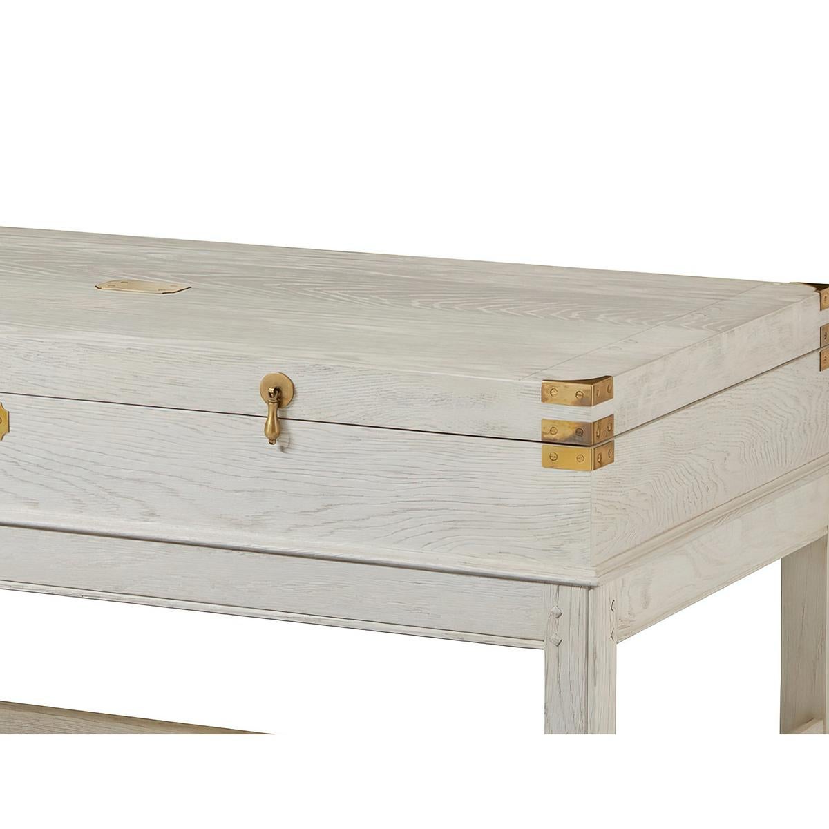 Modern Campaign Coffee Table with a white painted oak finish, with interior storage, brass hardware and mounts in the style of an antique English campaign case. On a stretcher base. 

Dimensions: 48.75