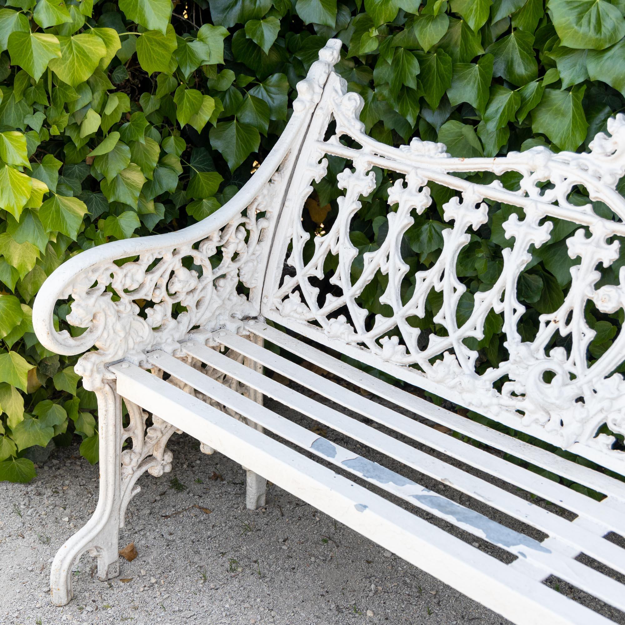 White lacquered cast iron garden bench in the neo-Gothic style of late 19th century Victorian garden furniture. The central medallion shows the Mexican heraldic eagle circumscribed by 