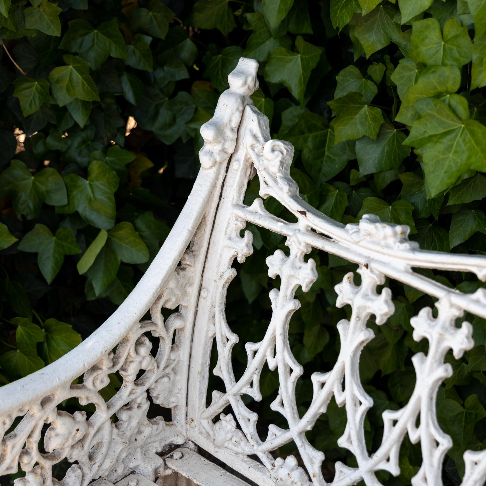 White lacquered cast iron garden bench in the neo-Gothic style of late 19th century Victorian garden furniture. The central medallion shows the Mexican heraldic eagle circumscribed by 