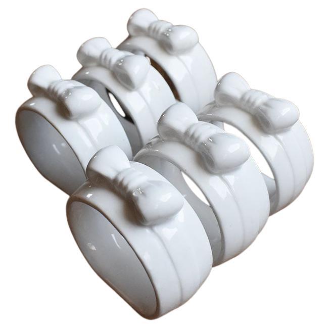 A set of six porcelain ribbon motif napkin rings. This set will be a gorgeous addition to any table setting. Each piece is glazed in a crisp white and features a bow tied at the top. Use with your favorite napkins at your next dinner party.