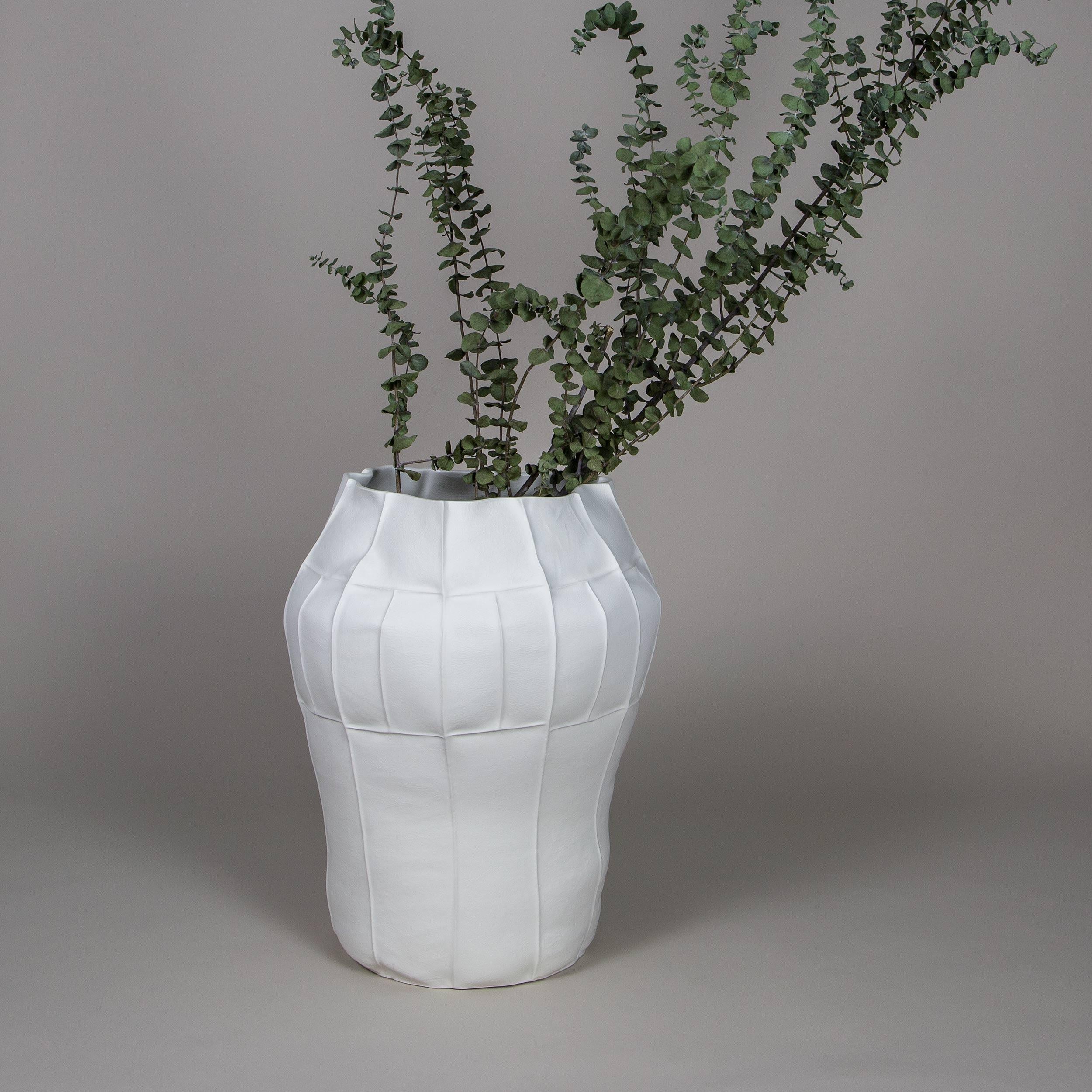 A tall oversized porcelain vessel with leather textured exterior surface and clear glazed interior. As a result of the production process each item is one-of-a-kind. 

A multitude of small leather panels are sewn together to create the leather mold