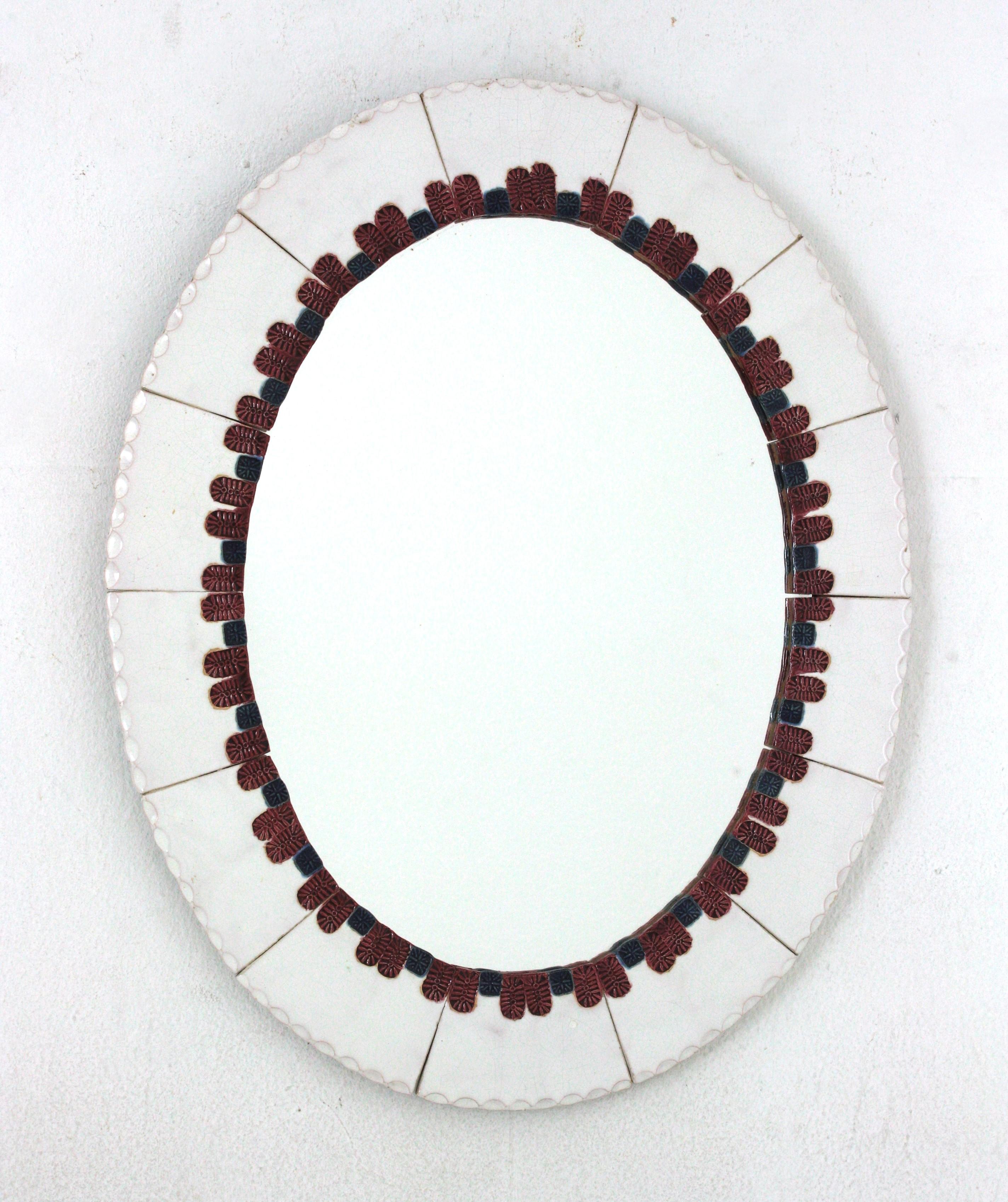 Auffälliger Mid-Century Modern Keramikspiegel. Hergestellt in Spanien, 1960er Jahre.
Ovale Form und bunter Rahmen.
Sie besteht aus glasierten Keramikfliesen in weißer Farbe. Ein dekoratives Muster in Blau und Rosarot umgibt den Glasspiegel.
Dieser