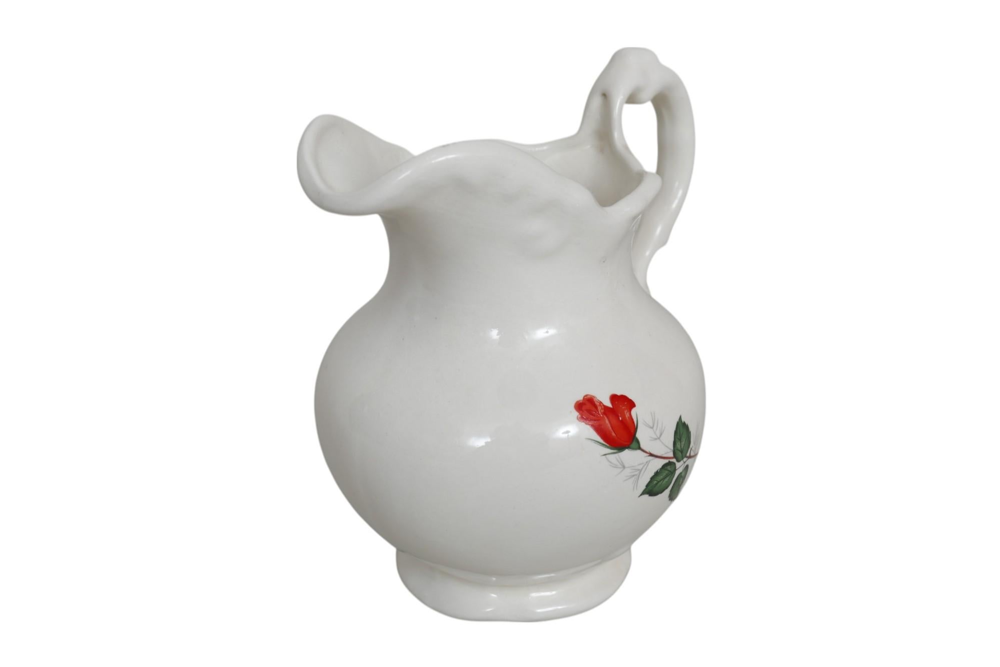 Pichet en céramique émaillée blanche, décoré sur le côté gauche d'une seule rose rouge sur une fine tige à trois feuilles. La rose en transferware est peinte à la main sur le dessus avec des lignes et des points. Le bec verseur en forme de serpentin