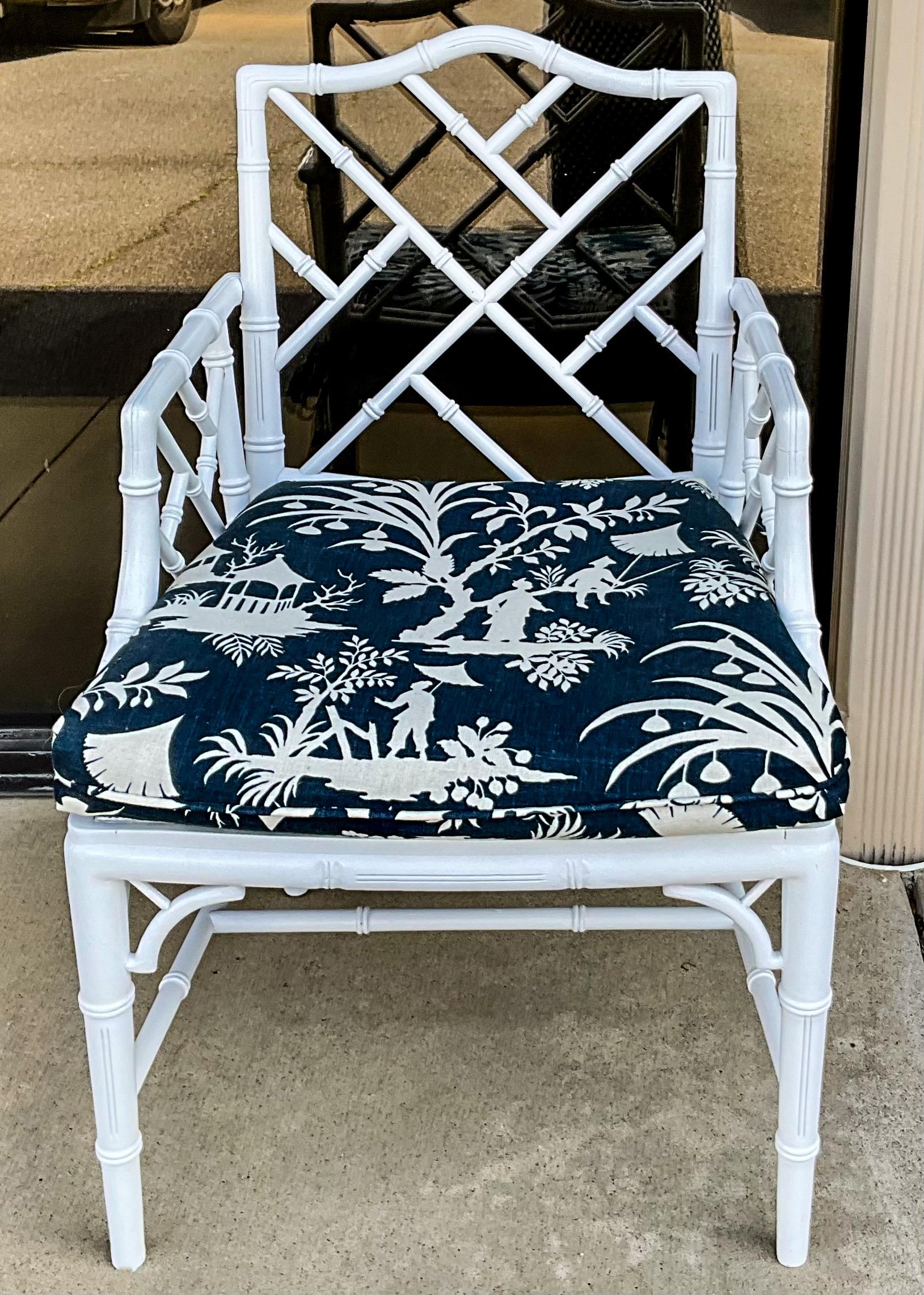 This is a 1970s white lacquer Chinese Chippendale style faux bamboo arm chair. The finish is a white lacquer. The seat is caned with a navy and white cotton linen blend chinoiserie. The fabric is the “South Seas” pattern by Thaibaut. It is unmarked