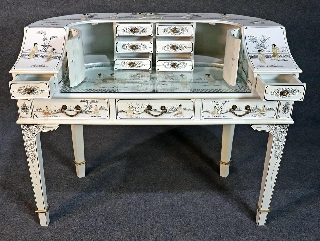 White chinoiserie carlton house desk with a glass top on the writing surface, 11 drawers, and 2 doors.