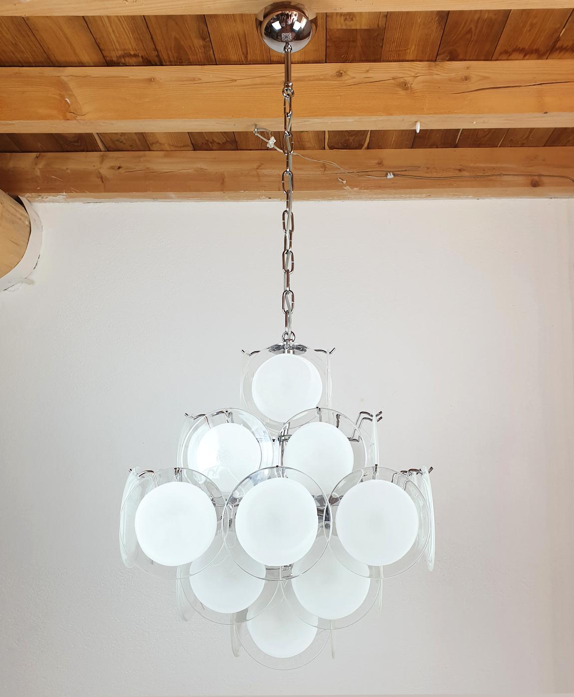 Vintage Modern hand blown murano glass chandelier, by Vistosi, Italy, circa 1980s.
The Mid-Century Modern chandelier is made of white and clear Murano glass discs on a chrome frame.
The shape is pyramidal, giving it a Mid Mod style.
It has 6