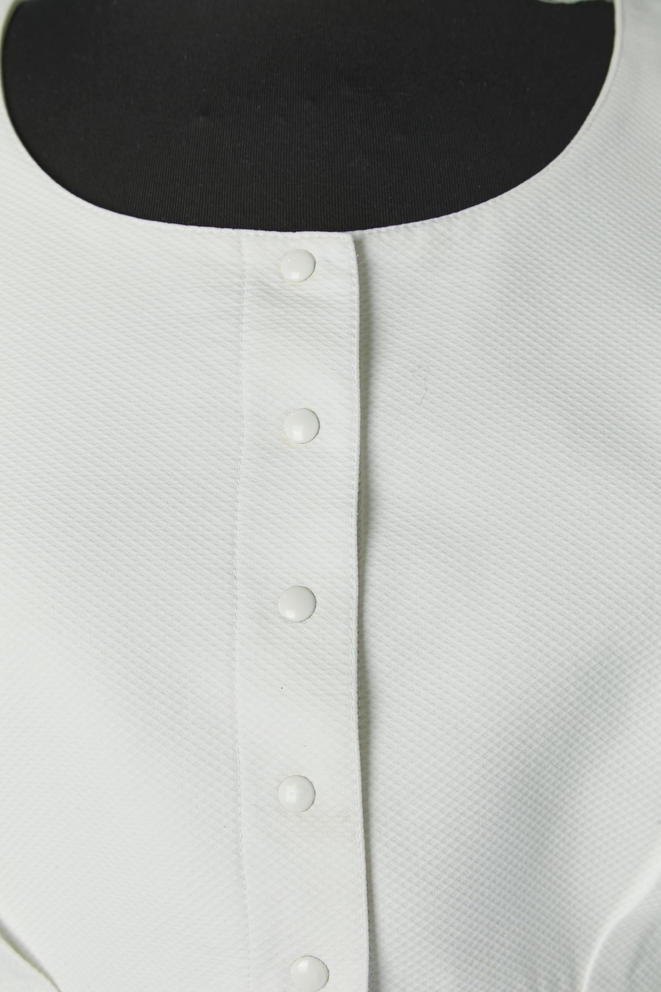 Abito-gonna in piqué di cotone bianco con fiocco sul retro della giacca e volant. Fodera in cotone. Chiusura a scatto sul centro della parte anteriore. Tasca su entrambi i lati. 
TAGLIA 38 (Fr) M 