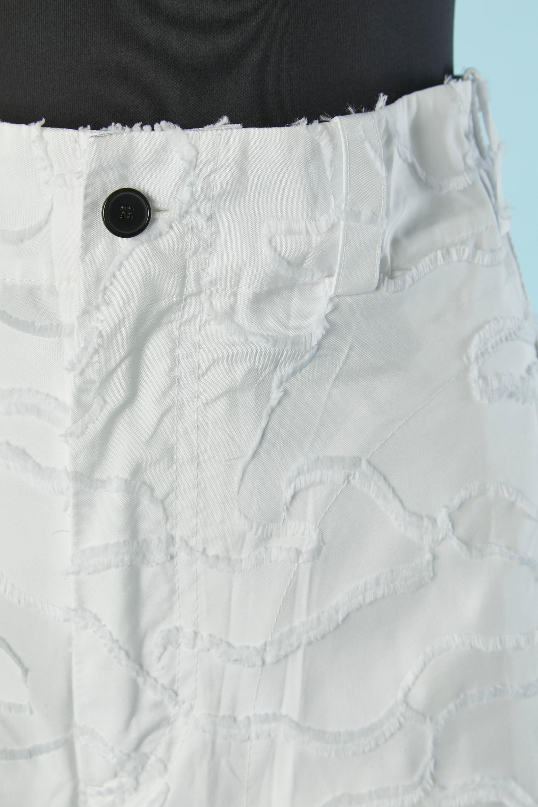 Pantalón blanco de algodón con aplicación de flecos de hilo y tira de nailon de la marca a ambos lados. Cierre a presión en el lateral. Cierre de botón, ojal y cremallera en la parte superior central delantera. 2 bolsillos delante y uno detrás. Lazo