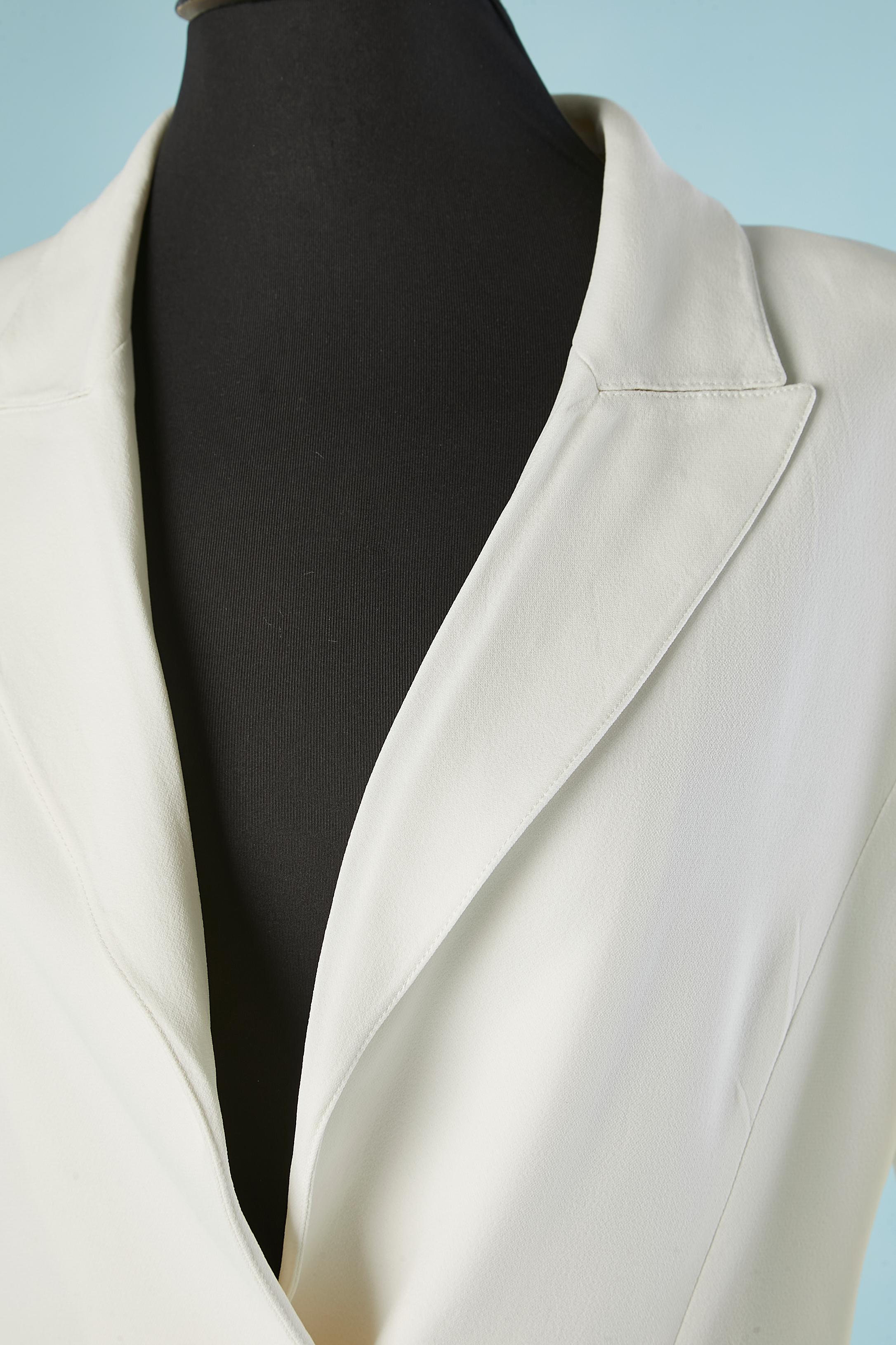 Combinaison-pantalon en crêpe blanc . La veste à simple boutonnage se ferme à l'aide d'un bouton en nacre. Pad d'épaule ; fendu des deux côtés, longueur= 27 cm
Doublure en soie. 
Taille de la veste= 42 (It) 8 (US) 
Taille du pantalon = 40 (It) 6