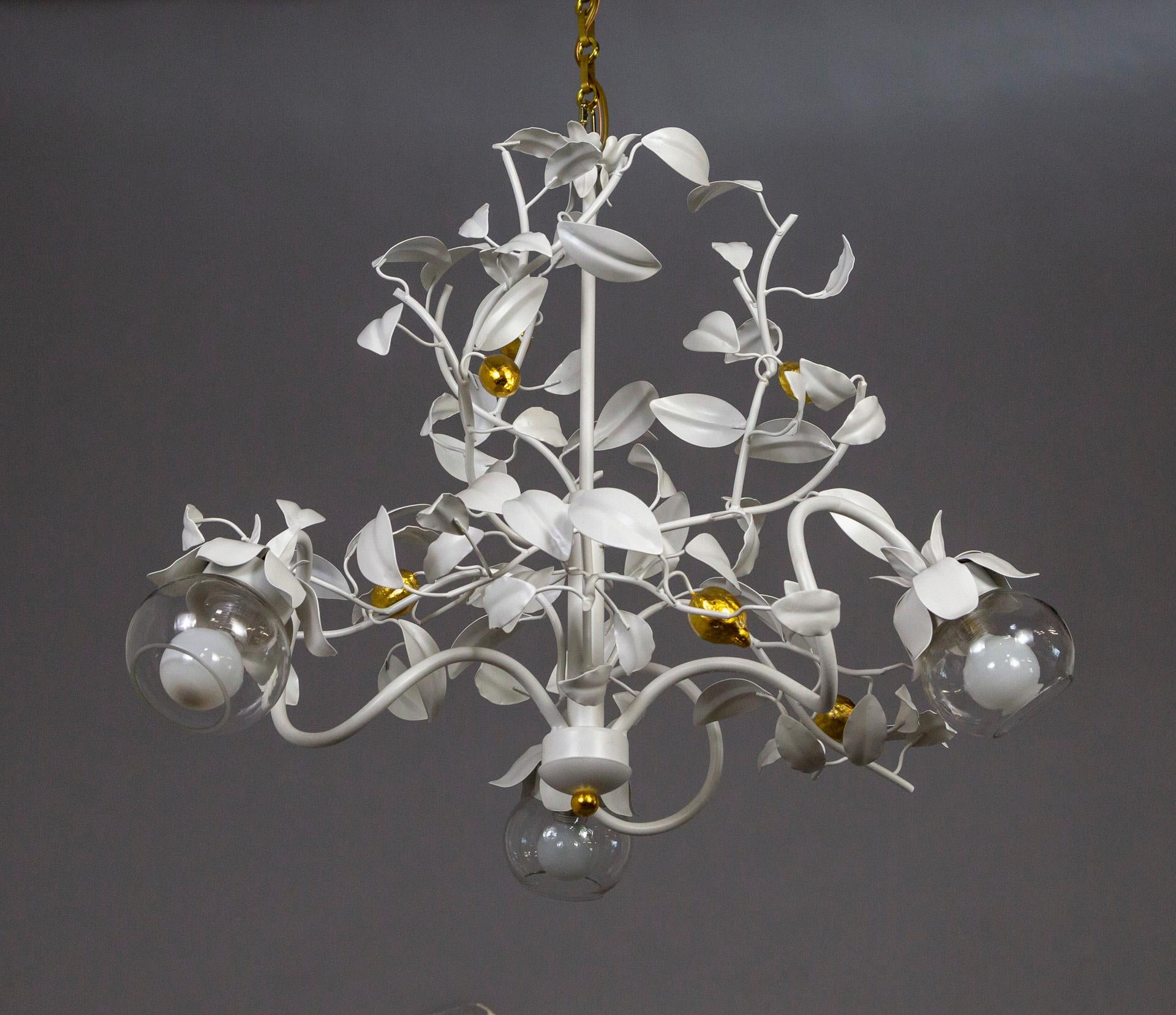 A newly restored, white lacquered chandelier with 3 curling arms and many swooping vines filled with leaves around the center stem and accented with gilded lemons throughout. The 3 lights have glass globe shades and candelabra sockets; with a long