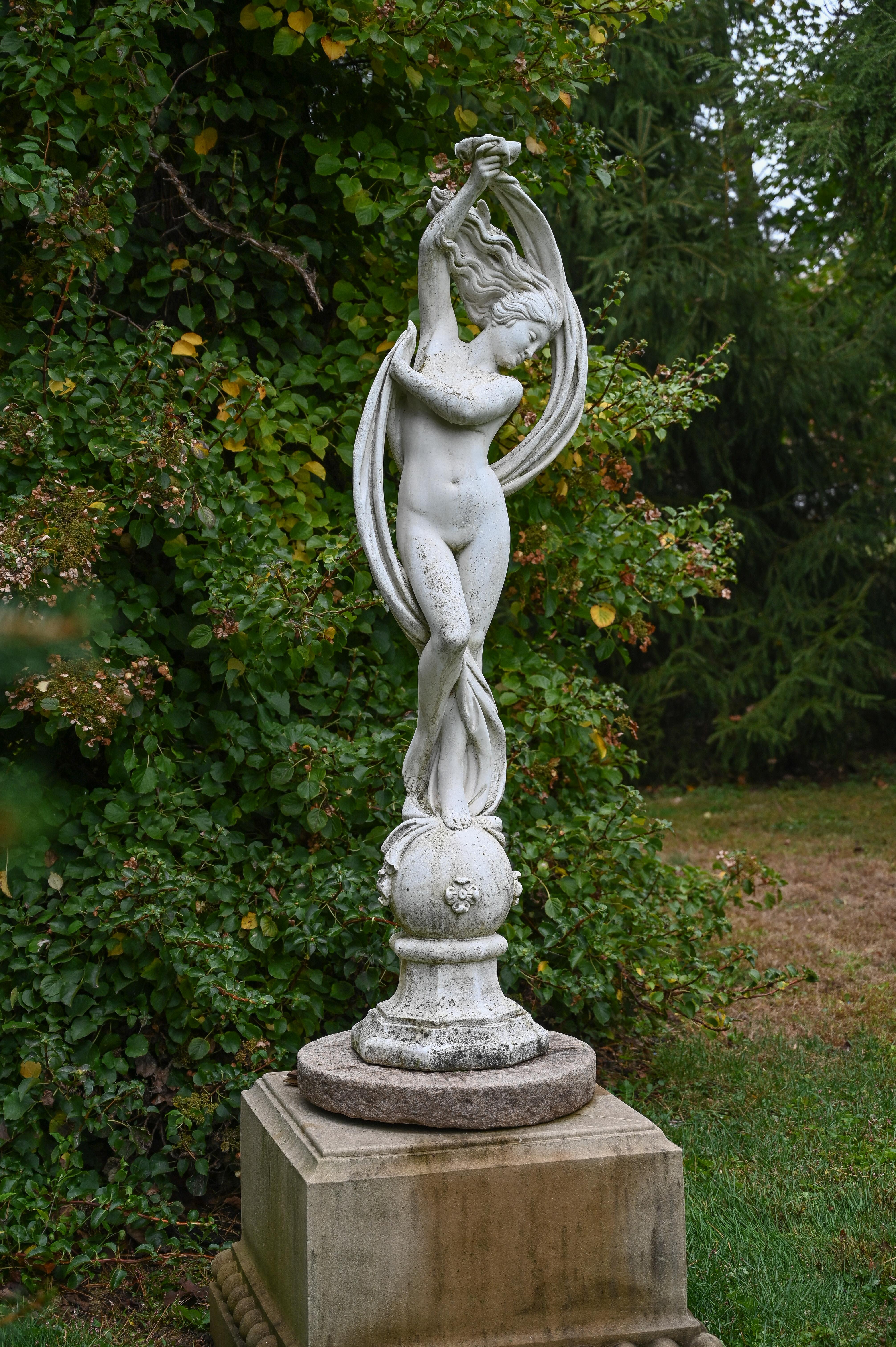A composition stone figure of a maiden with upswept hair and a long flowing ribbon of fabric, the maiden standing on a sphere raised on octagonal base, Italian, circa 1960. Marked “PAPINI A” for the Papini (Agostino SNC) company in the Rignano