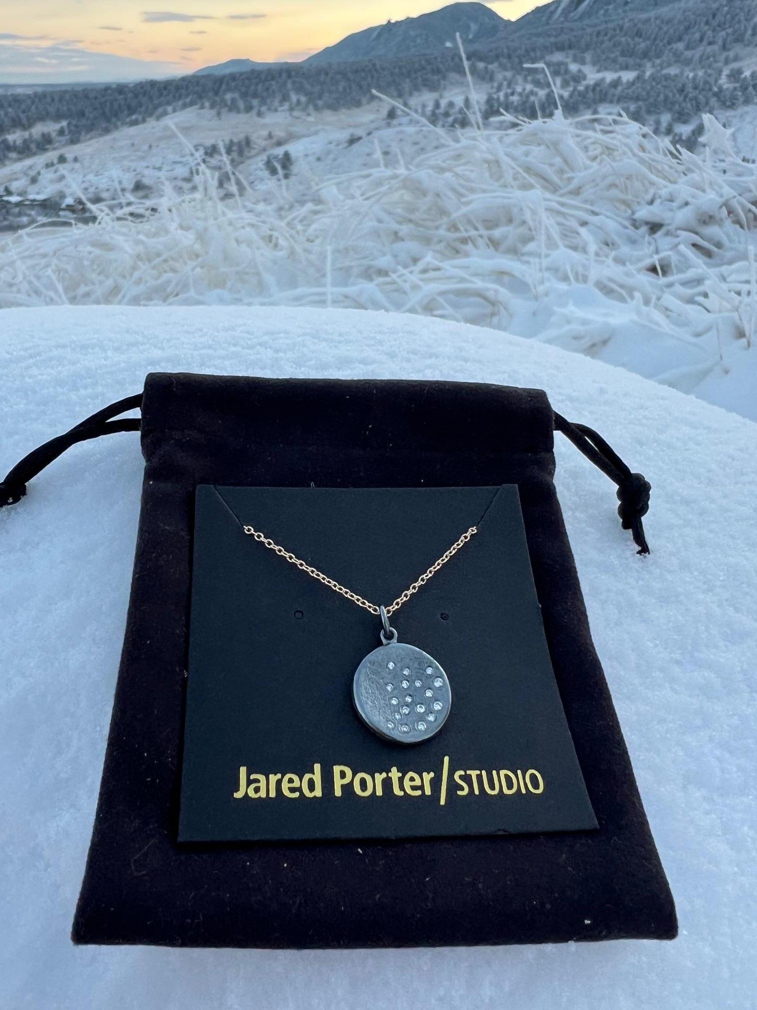 Beautiful pendant hand fabricated by Jared Porter Studio.

The inspiration behind this every day wearing necklace was to give the feeling of snowfall or a bright starry nights sky.  

The disc is sterling silver with a dark patina (oxidized) finish
