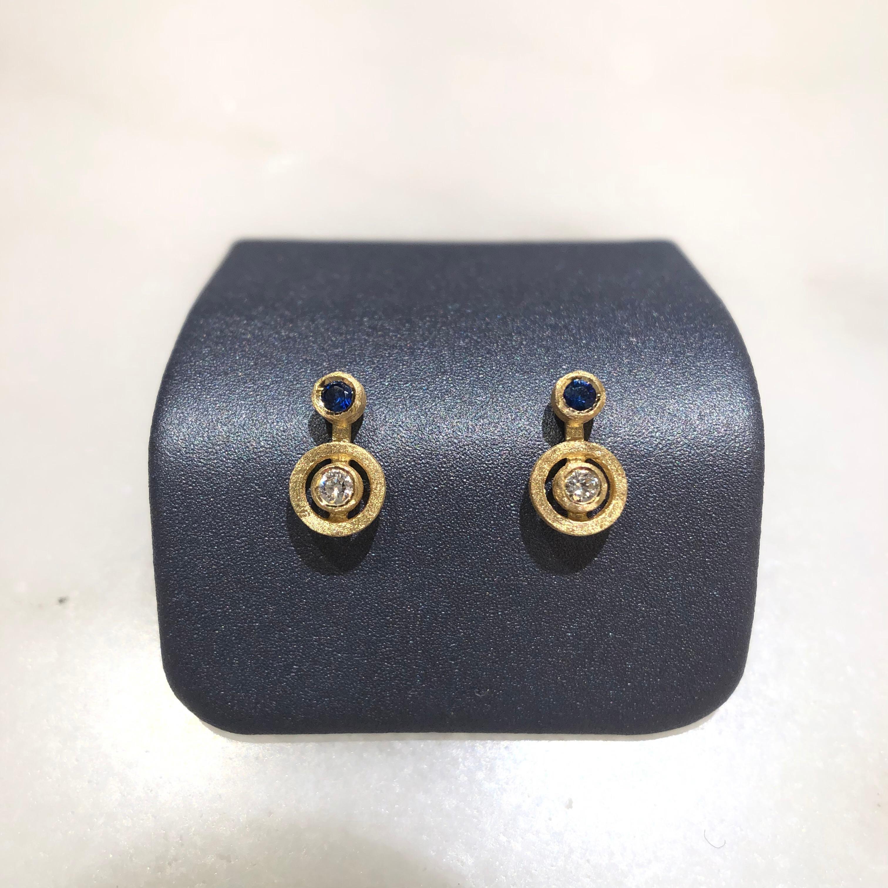 Nova Stud Earrings handcrafted in London by jewelry artist Shimell and Madden in satin-finished 18k yellow gold with 0.08 total carats of round brilliant-cut white diamonds and two vibrant blue sapphires, all bezel-set and attached to central 18k