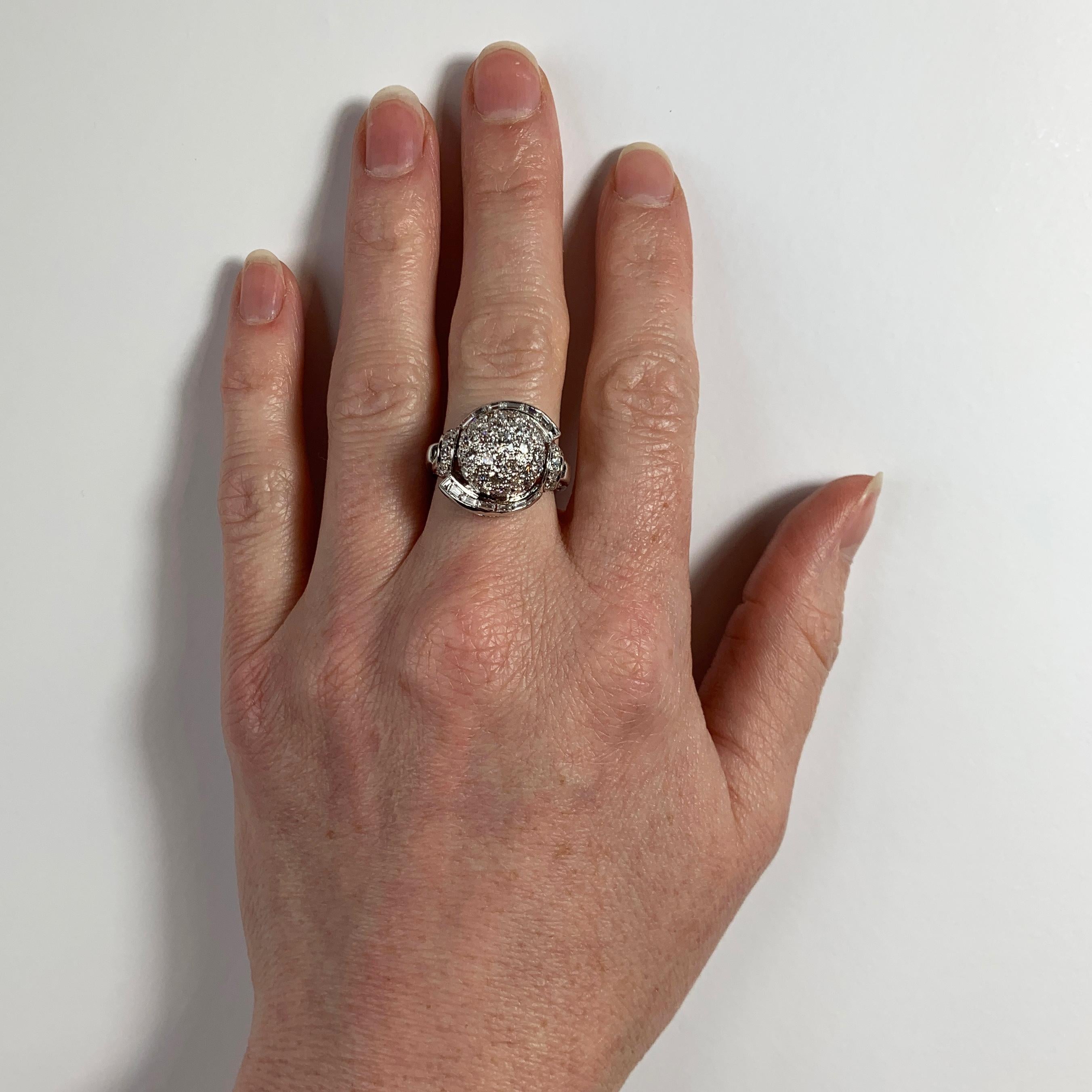 A platinum and white diamond cocktail ring designed as a dome with a curve of tapered baguette diamonds to each side and diamond set shoulders. The ring is set with 41 round brilliant cut white diamonds and 12 baguette cut diamonds. Unmarked but
