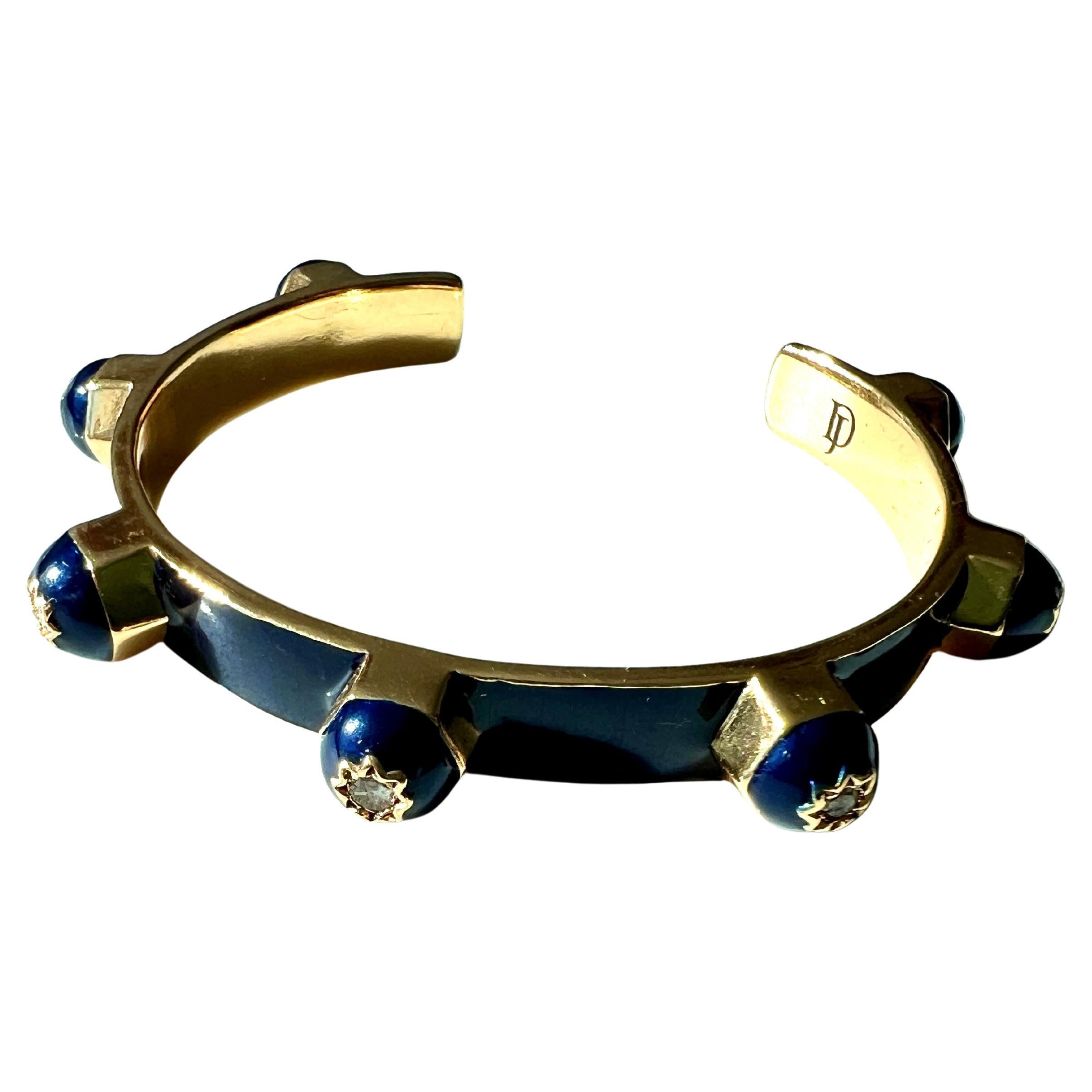 This royal blue enamel cuff bracelet by J Dauphin features a bold open cuff design with engraved eight-pointed stars, each set with a natural white diamond. Crafted in 14k gold-plated brass, the piece reflects a fusion of Victorian influence,