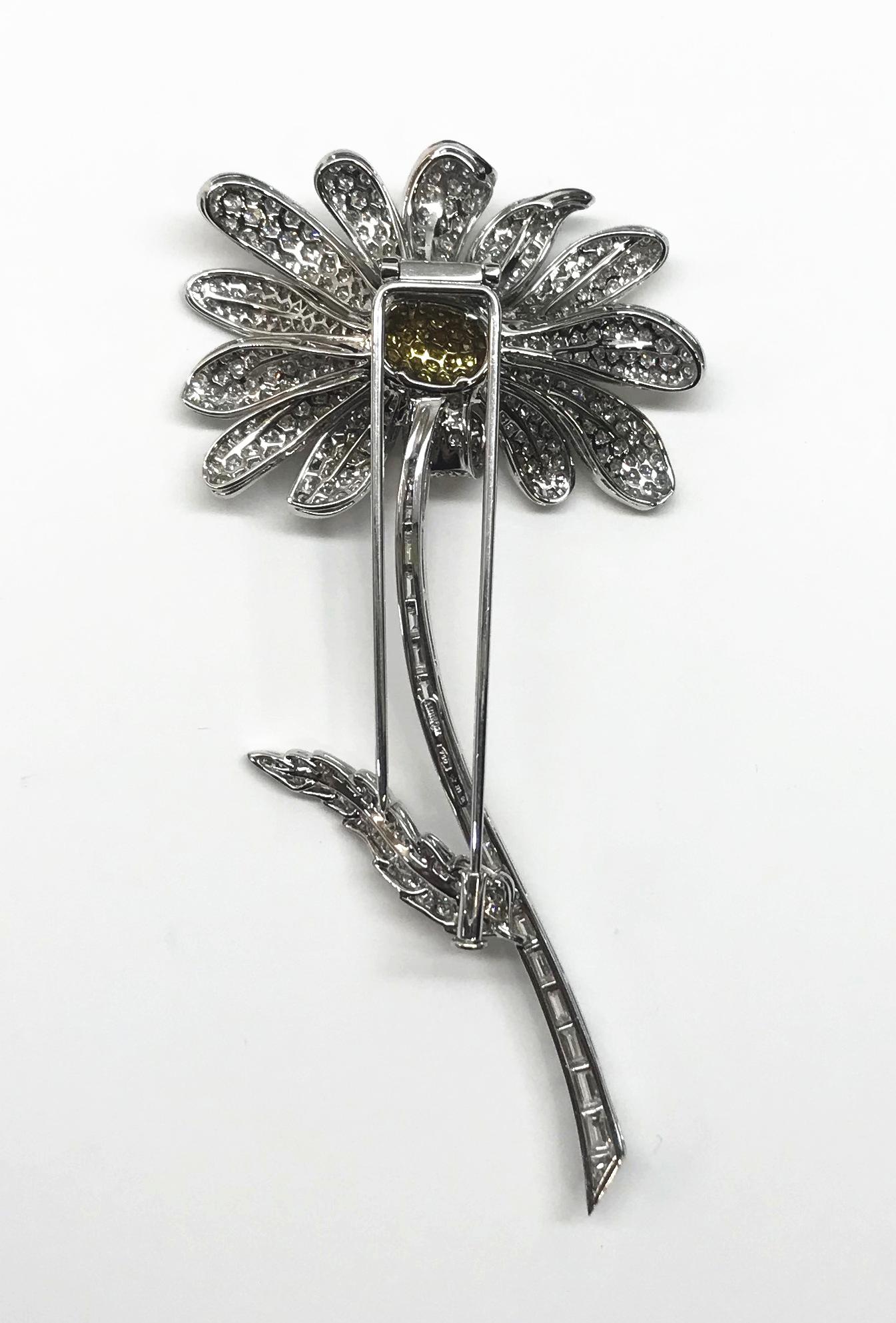 Striking “Daisy” Flower brooch having 13- white diamond pavé petals, set in 18K white gold, surrounding the center comprised of natural fancy yellow round brilliant cut diamonds set into 18K yellow gold. The blossom rests on a curved, channel-set