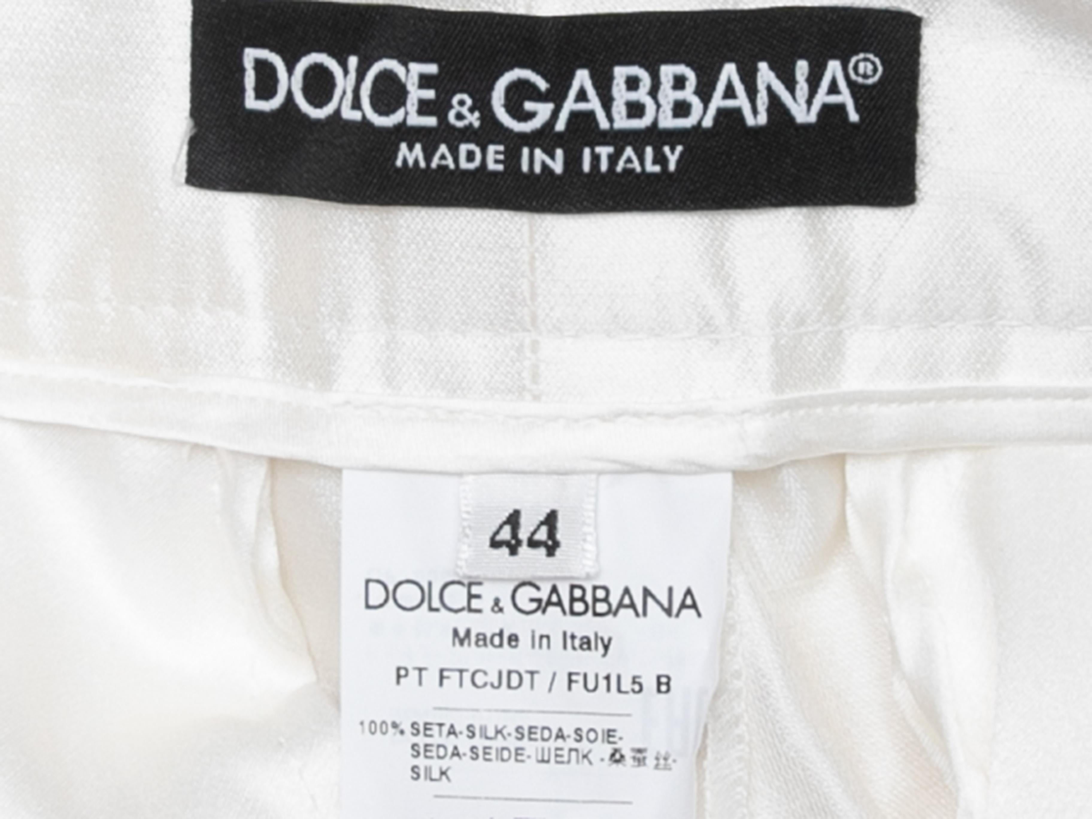 White shiny silk tapered trousers by Dolce & Gabbana. Dual back welt pockets. Zip and button closures at front. 28