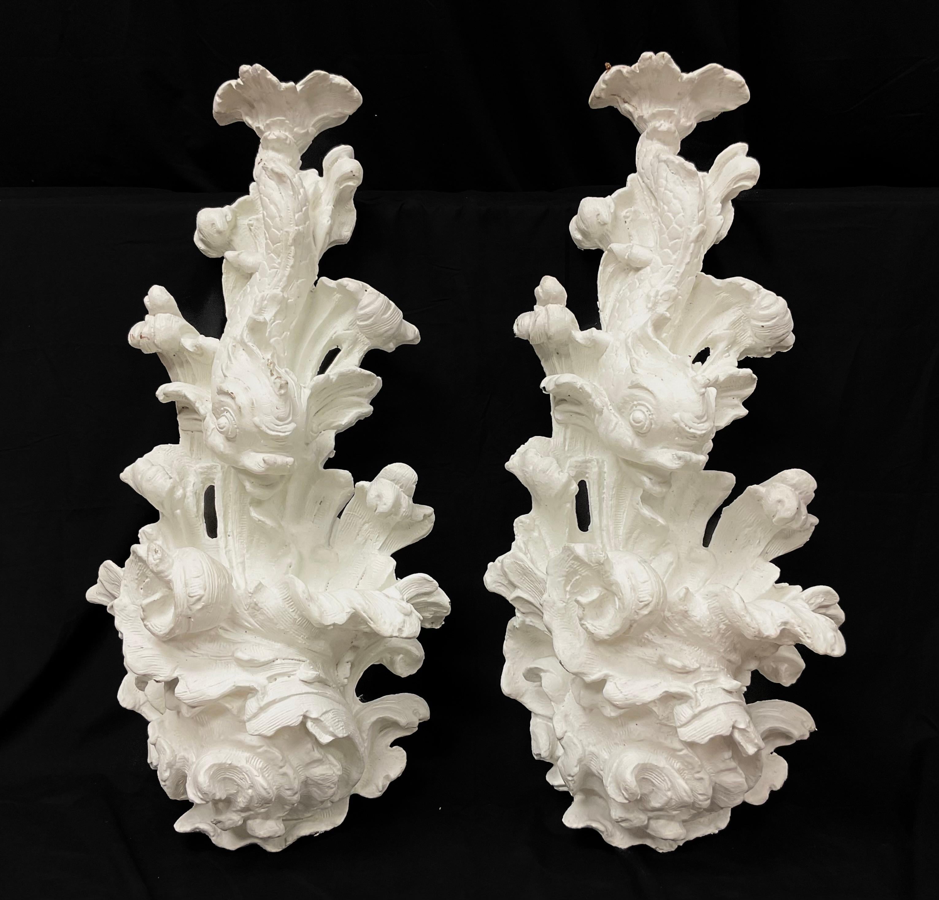 A Pair of White Dolphin Wall Appliqués made of plaster and fiberglass. These offer both sculptural detail and structural durability. The appliqués are rendered in a high-relief Rococo Revival style, the forms swirl with dynamic, wave-like movement