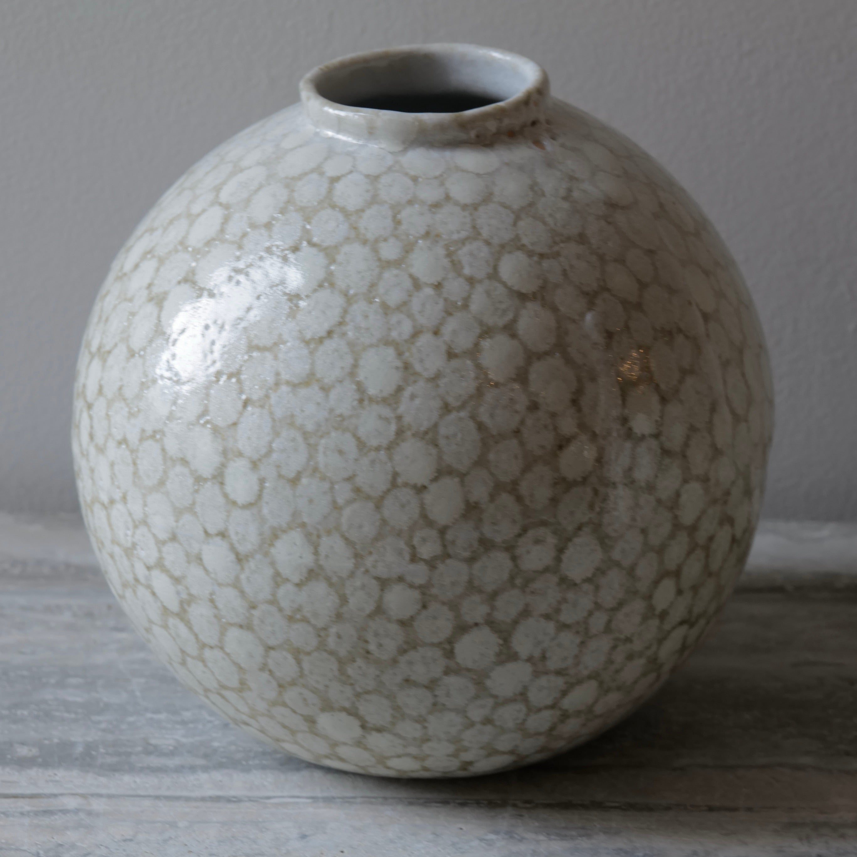 The White Dot Big Globe Vase is a striking statement piece that embodies modern craftsmanship and organic design. Hand-sculpted with a distinctive spherical form, this vase features a richly textured surface of raised white dots, creating a