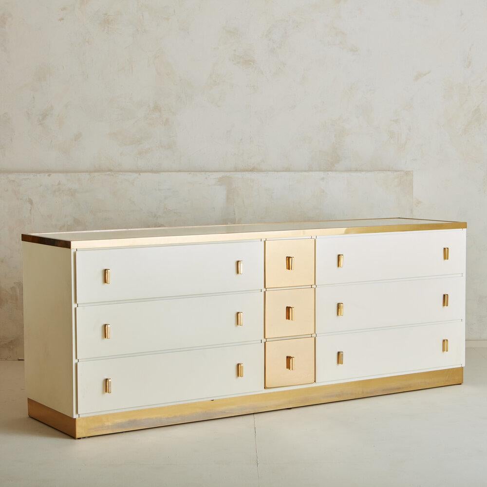 A refined white dresser in lacquered wood designed by Luciano Frigerio for Frigerio Di Desio in the early 1970s. This dresser features brass trim lining the base and top. Each drawer has angular brass handles. With six large drawers in addition to