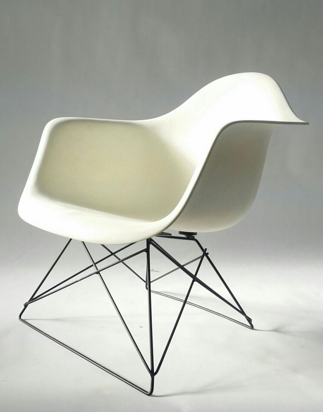 White Eames arm shell chair, produced by Herman Miller, circa 1972, on black 'cats cradle' base. We would describe this Eames fiberglass arm shell as 