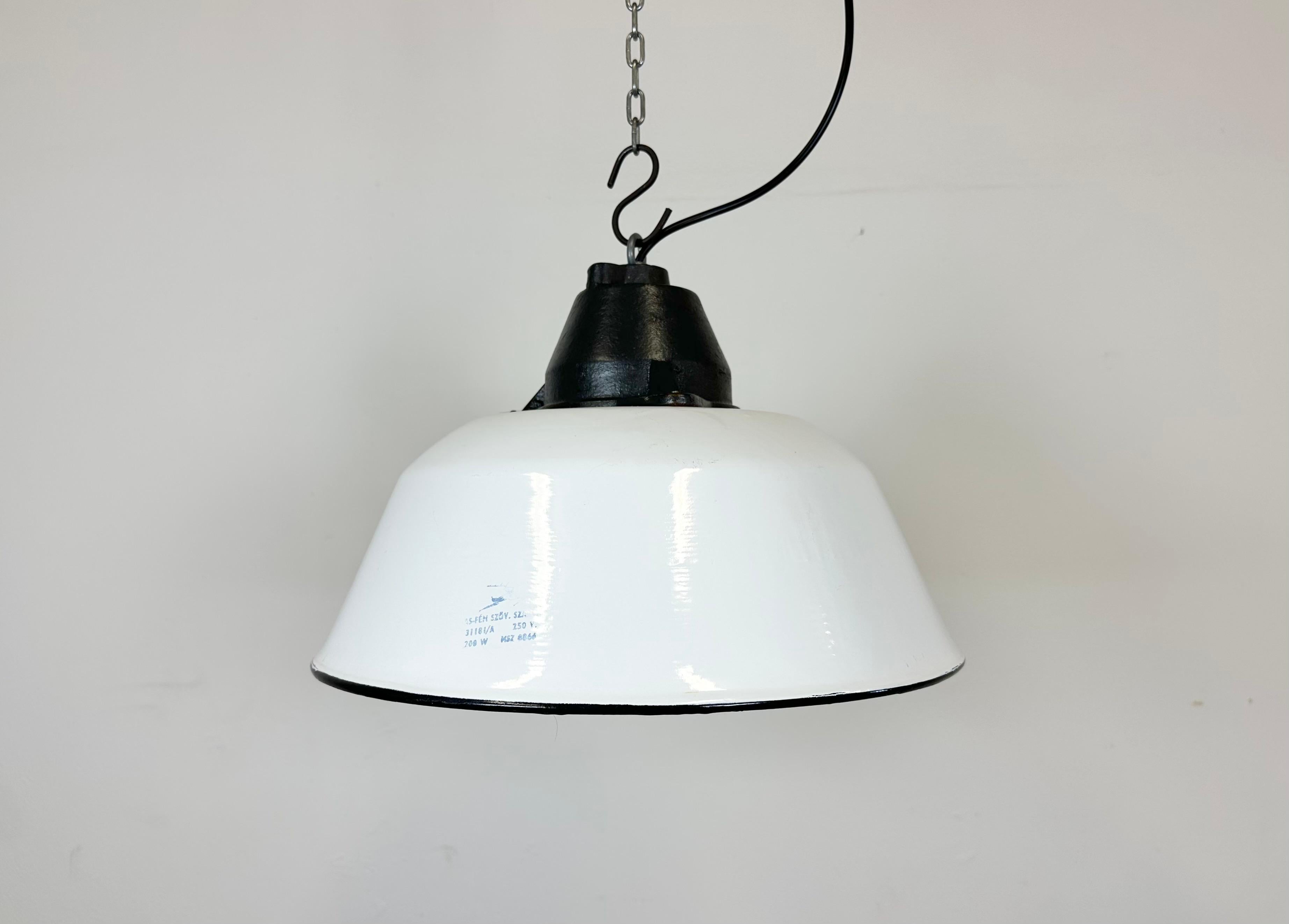 Industrial hanging lamp manufactured by Szarvasi Vas - Fém in Hungary during the 1960s. It features a white enamel shade with white enamel interior and a grey cast iron top. New porcelain socket requires standard E 27/E 26 light bulbs. New wire. The
